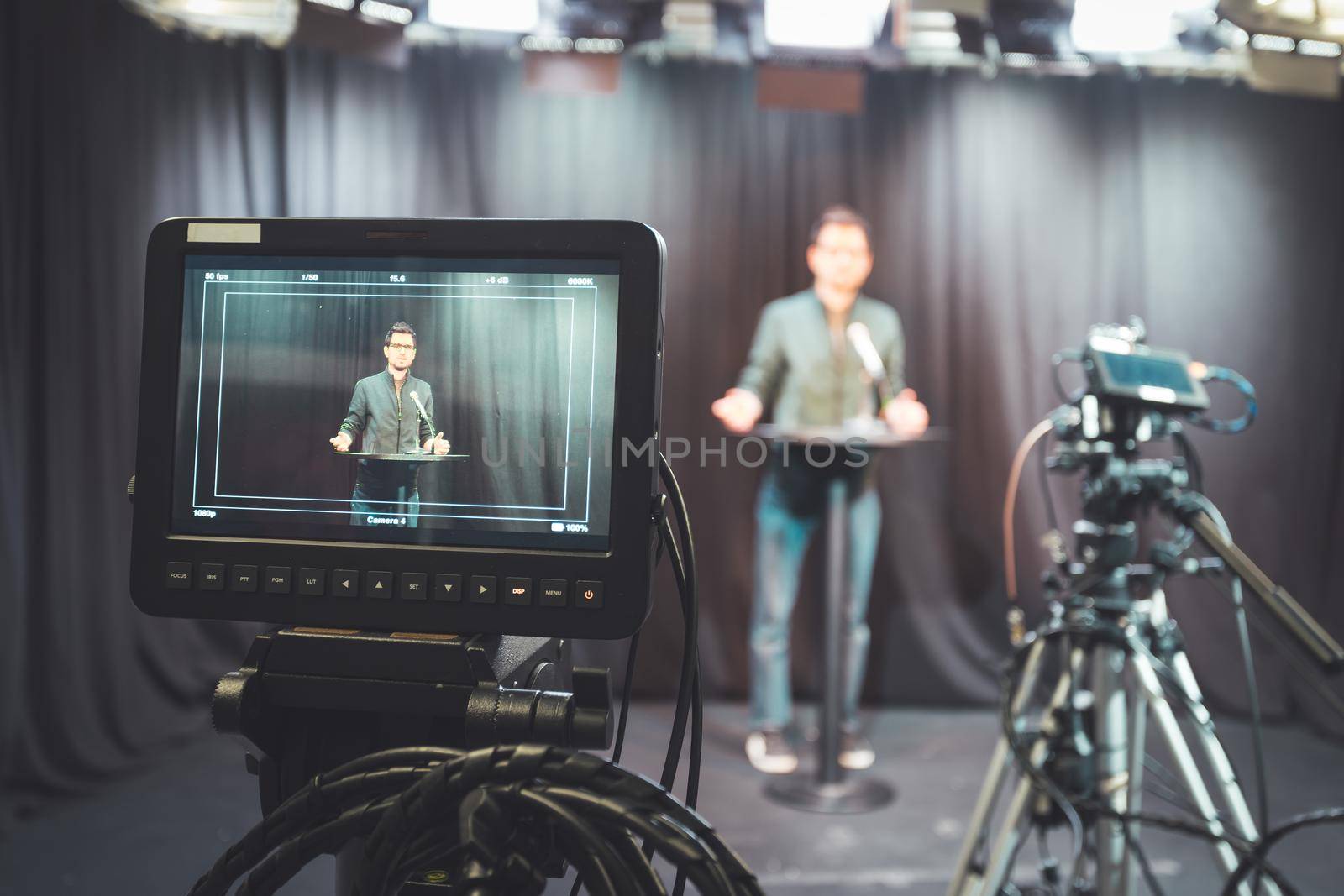 Young journalist in a television recording studio is talking into a microphone, blurry film cameras by Daxenbichler