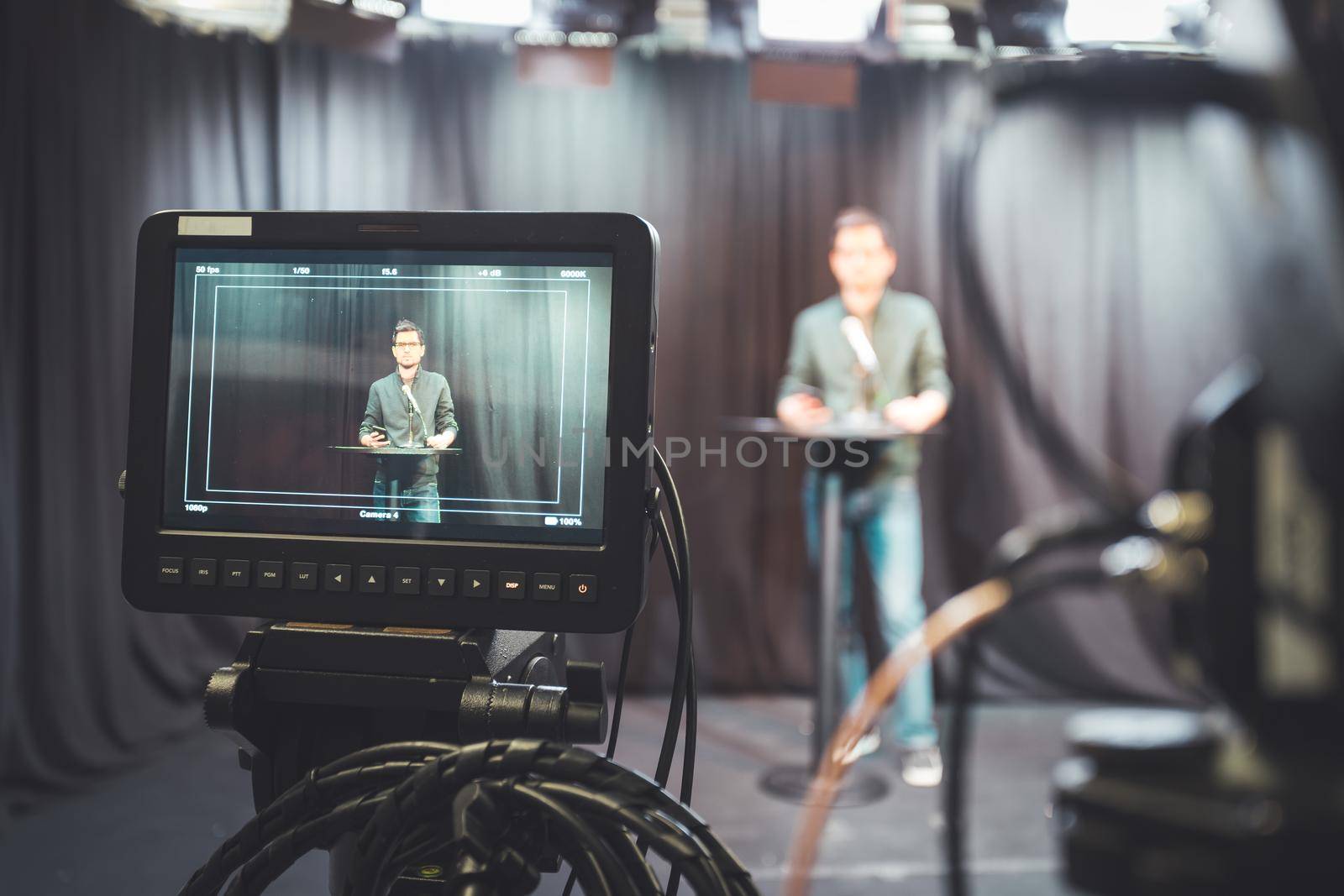 Young journalist in a television recording studio is talking into a microphone, blurry film cameras by Daxenbichler