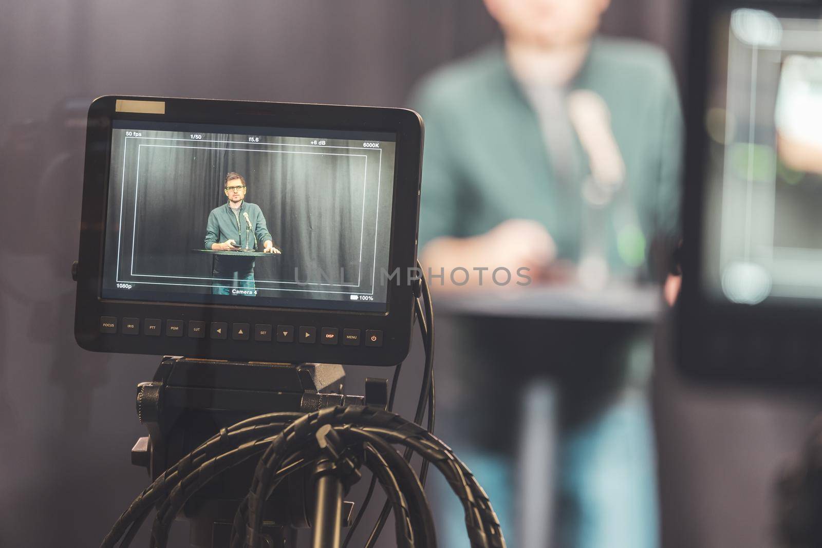 Male journalist in a television studio talks into a microphone, film cameras