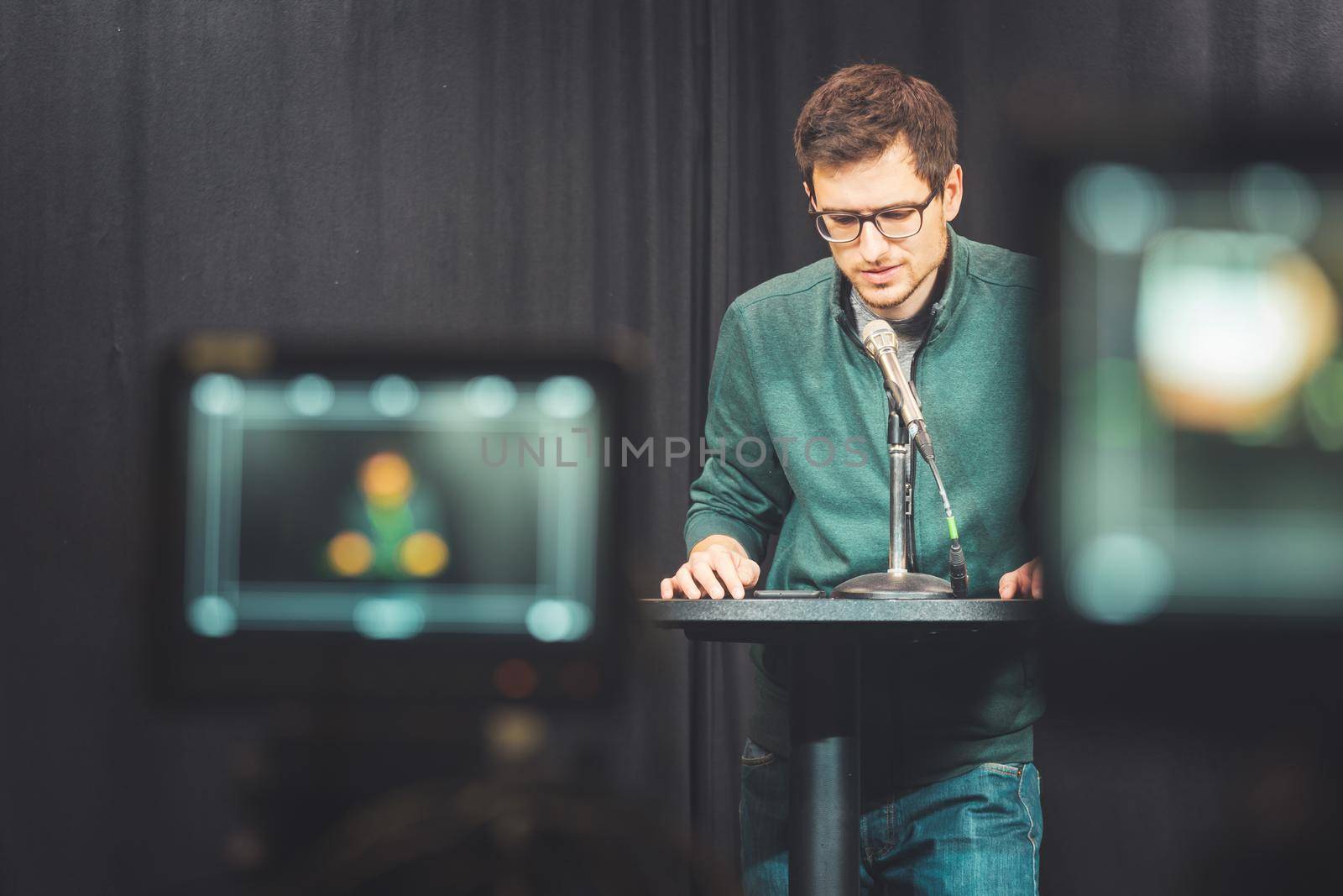 Male journalist in a television studio talks into a microphone, film cameras