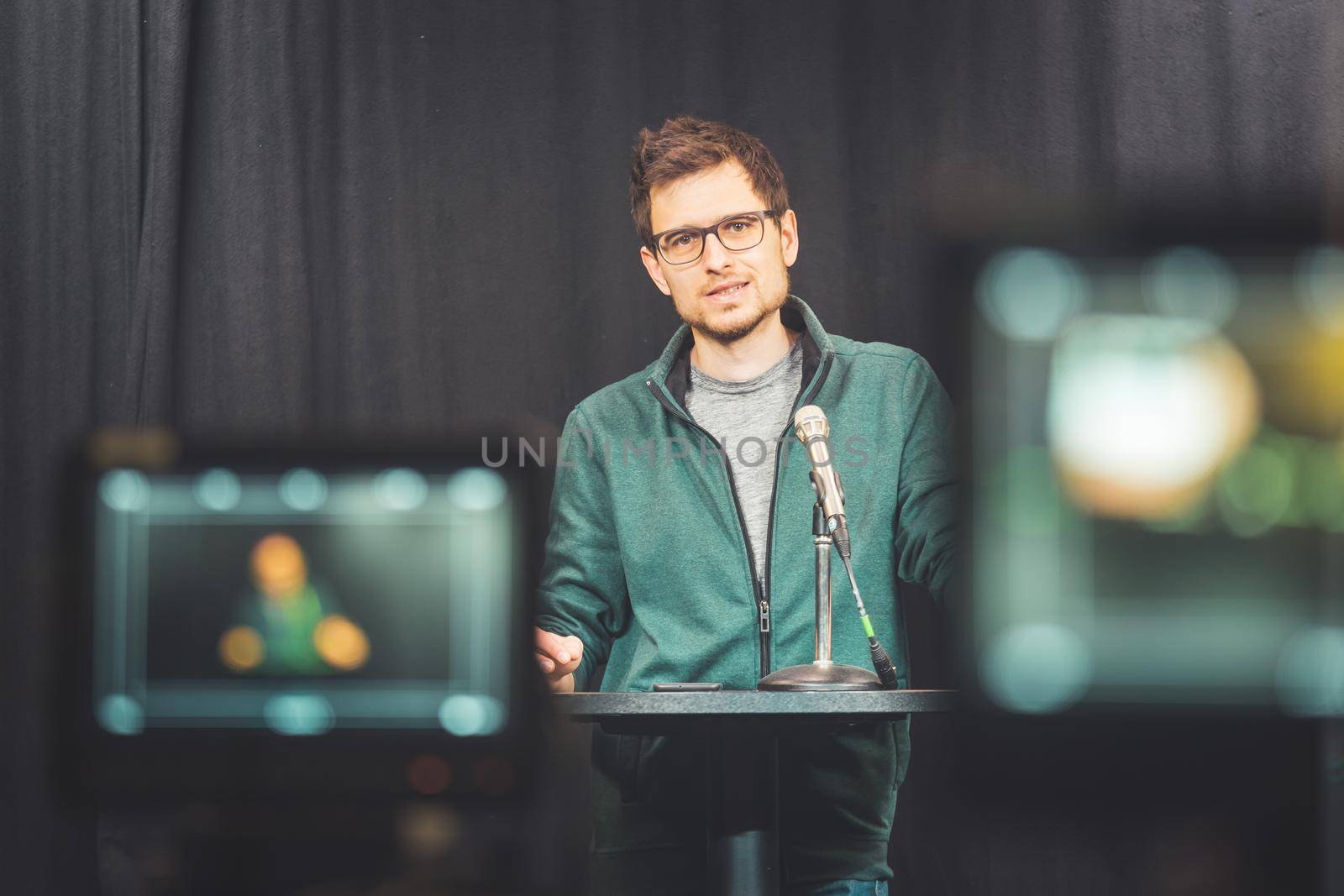Male journalist in a television studio talks into a microphone, film cameras