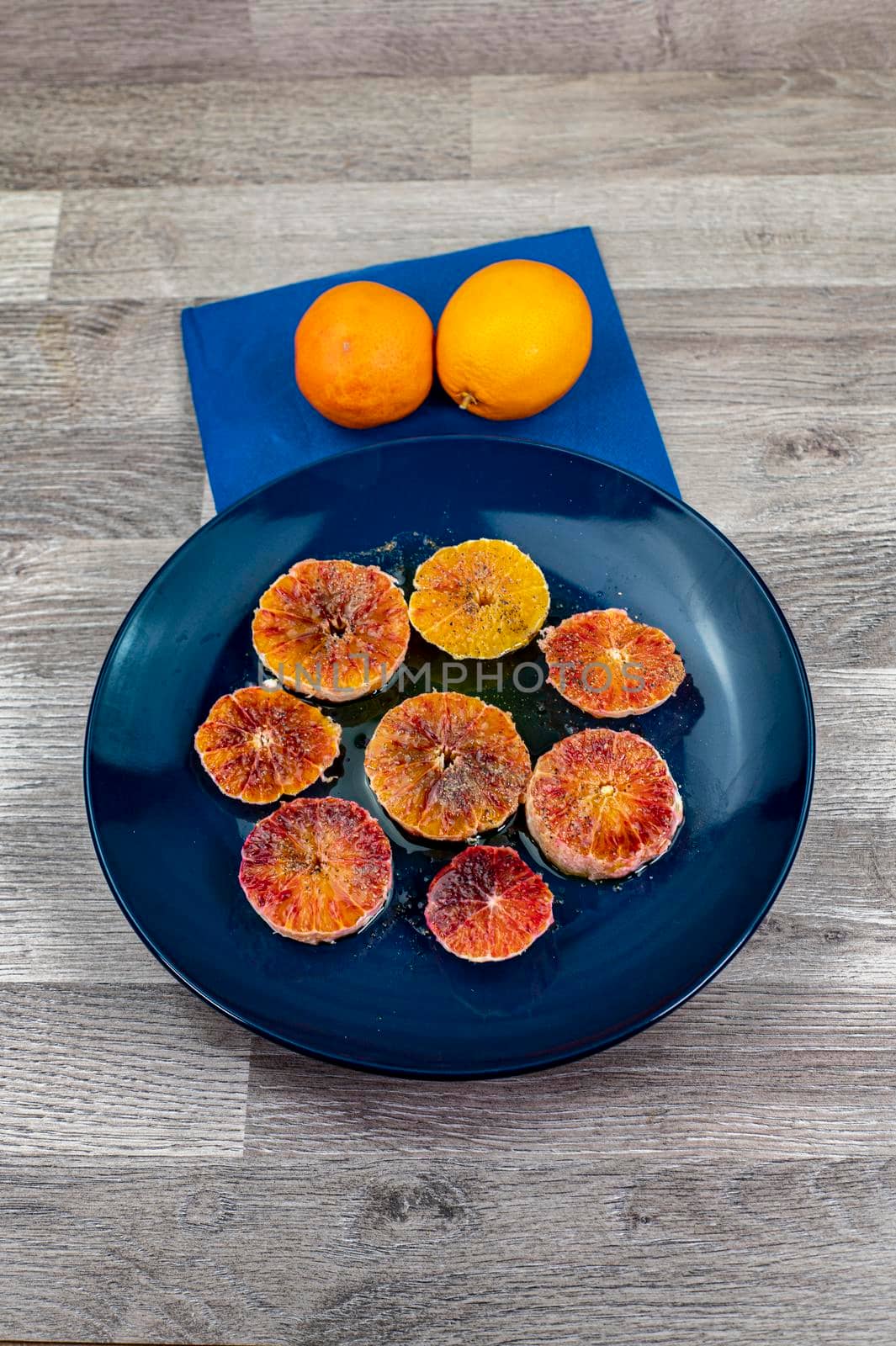 oranges seasoned with oil salt and pepper on a blue plate and wooden background oranges