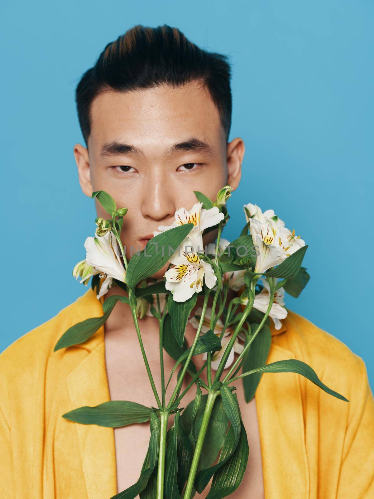 Cute Korean man in a yellow coat with a bouquet of white flowers on a blue background model by SHOTPRIME