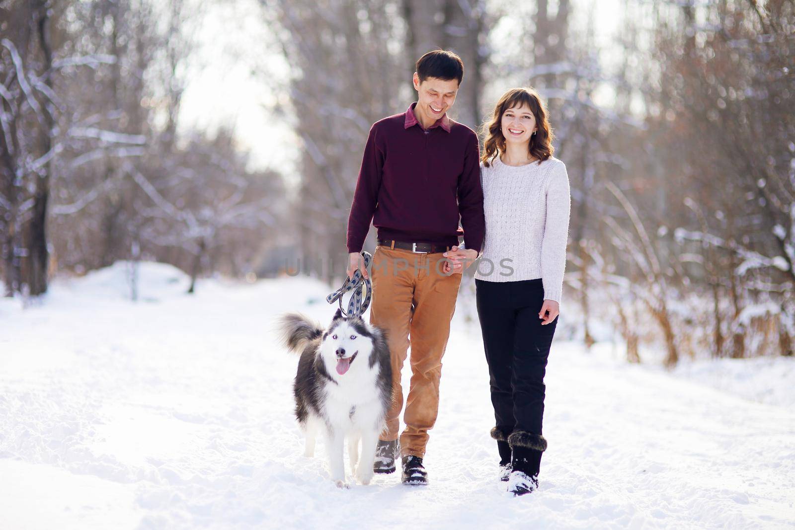 Young couple smiling and having fun in winter park with their husky dog.