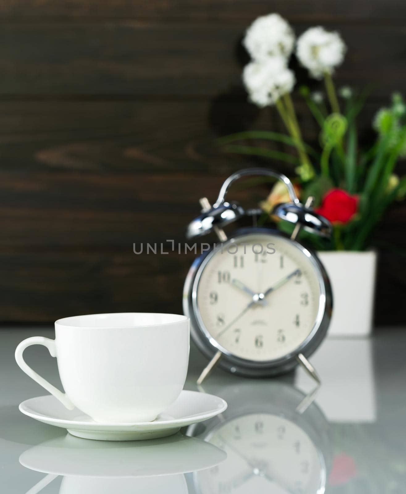 White coffee cup and alarm clock with Artificial flower vase bouquet on table