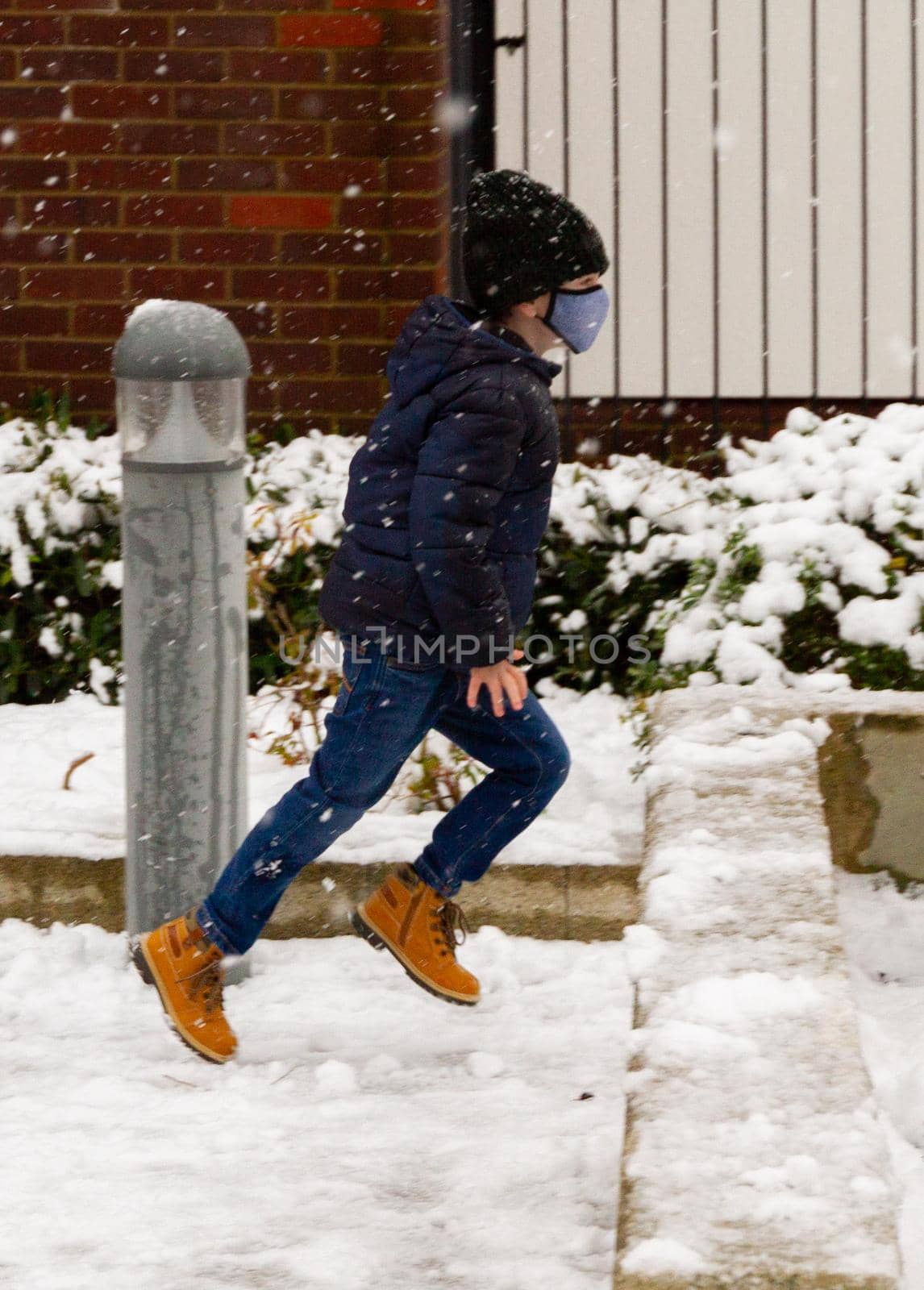 A cute boy wearing a black hat and a blue face mask running in the snow