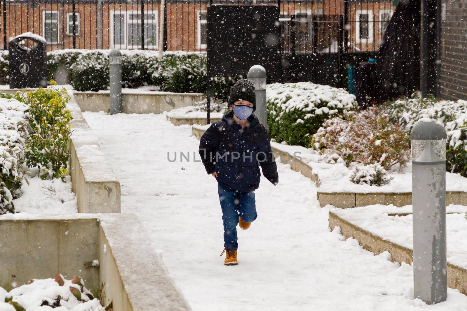 A cute boy wearing a black hat and a blue face mask running in the snow