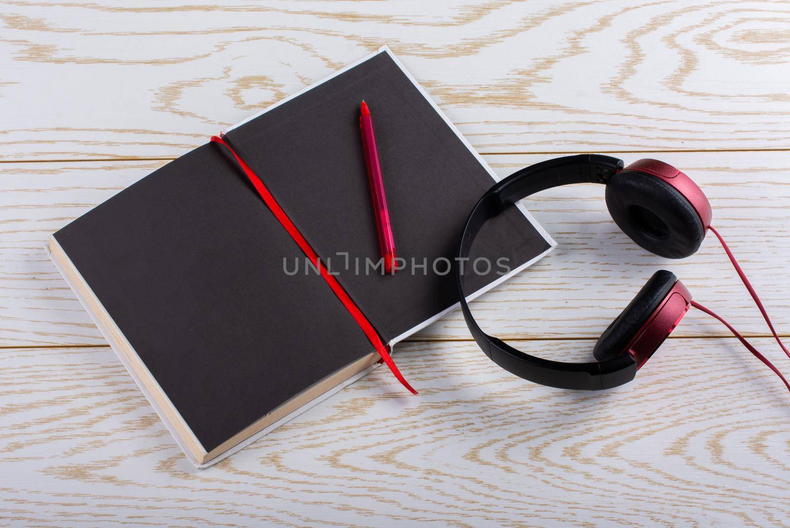 Red headphones, notebook, pen on a wooden background