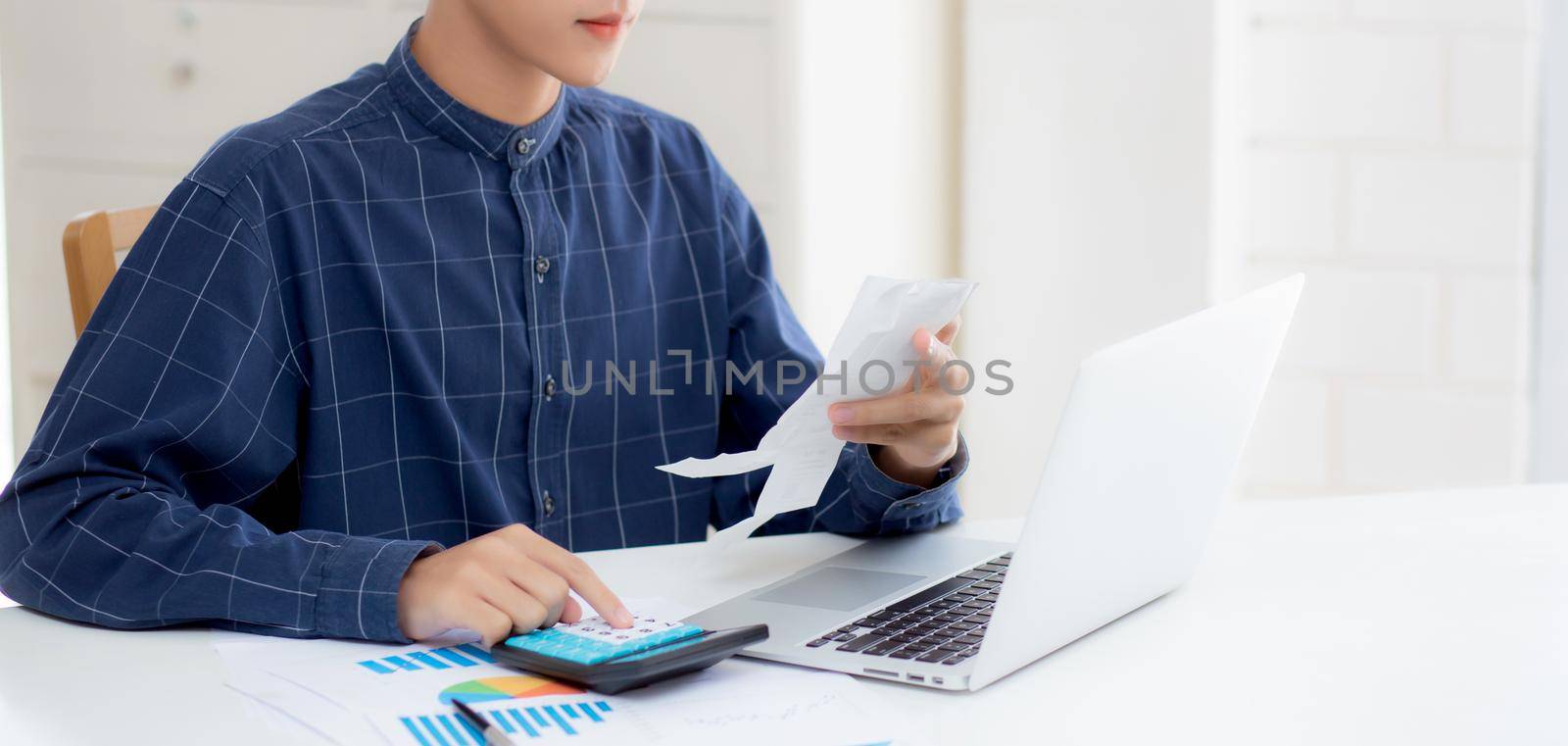 Young asian man calculating finance household with calculator on desk at home, male checking bill and success for saving expenses household, debt closure, tax and accounting, business concept.