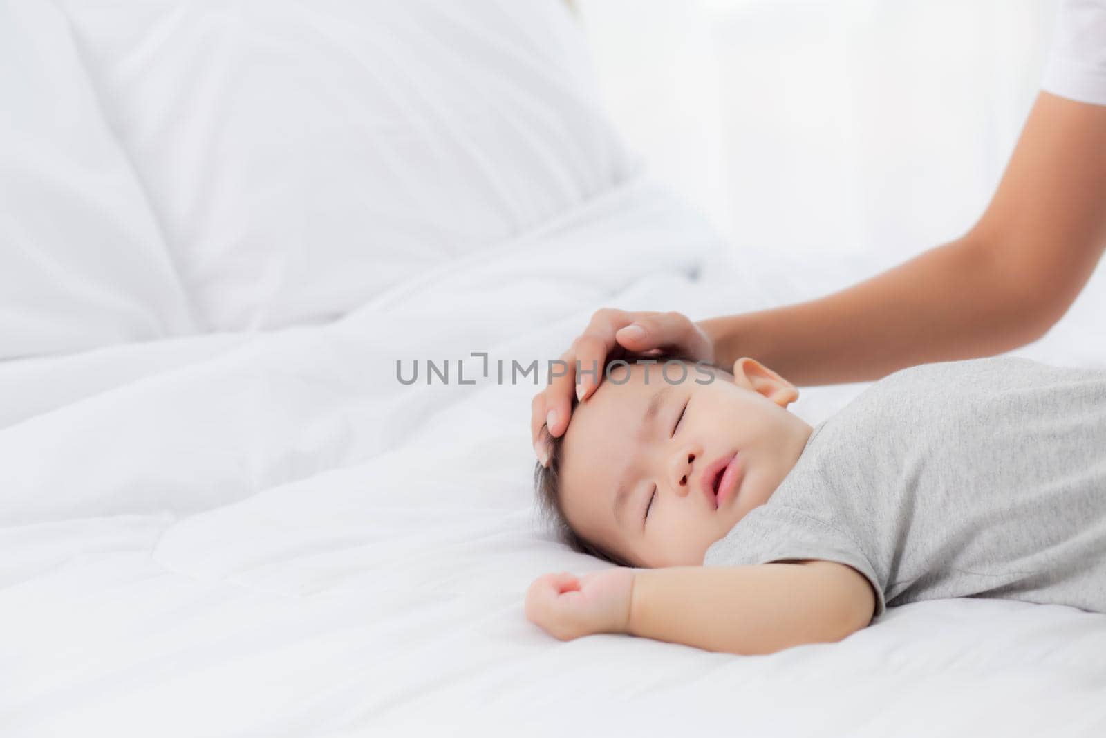 Young asian mother touch head of little baby girl with tender on bed in the bedroom, mom love newborn and care, woman with expression with child together, parent and daughter, family concept.