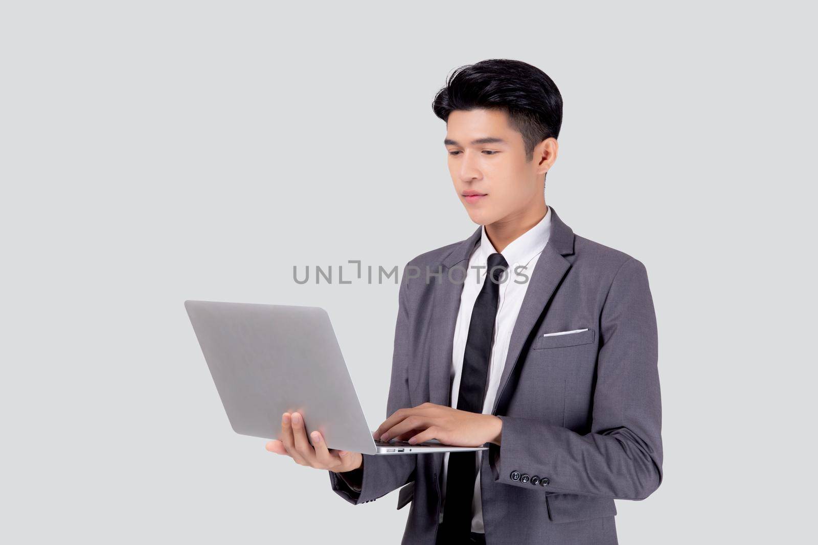 Young asian business man standing work on laptop computer to internet online isolated on white background, businessman confident and notebook, freelance with success, marketing and communication.