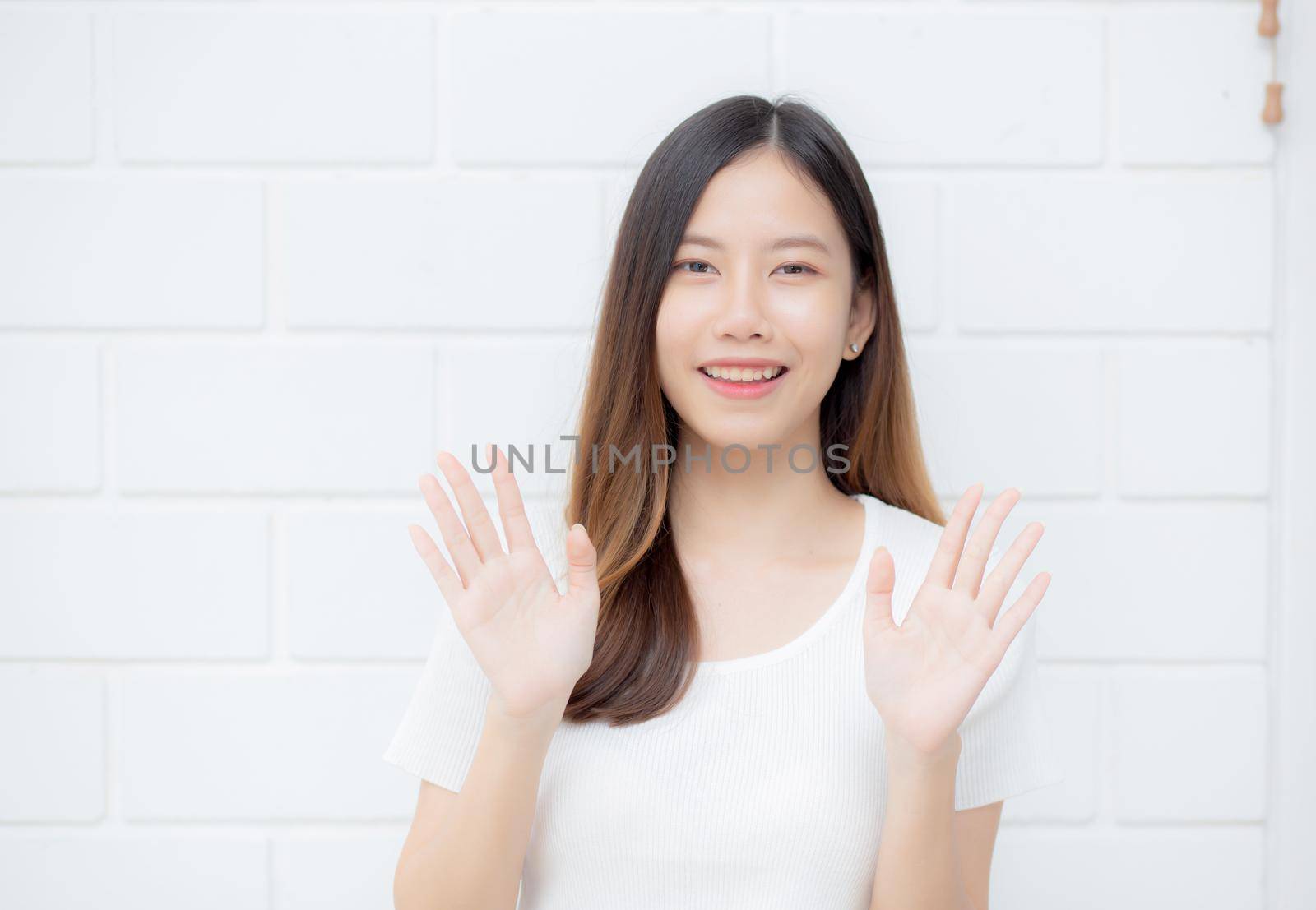 Beautiful young asian woman confident gesture say hello or greeting with waving her hand on cement background at home, friendly welcome, portrait girl cheerful expression happy and satisfied.
