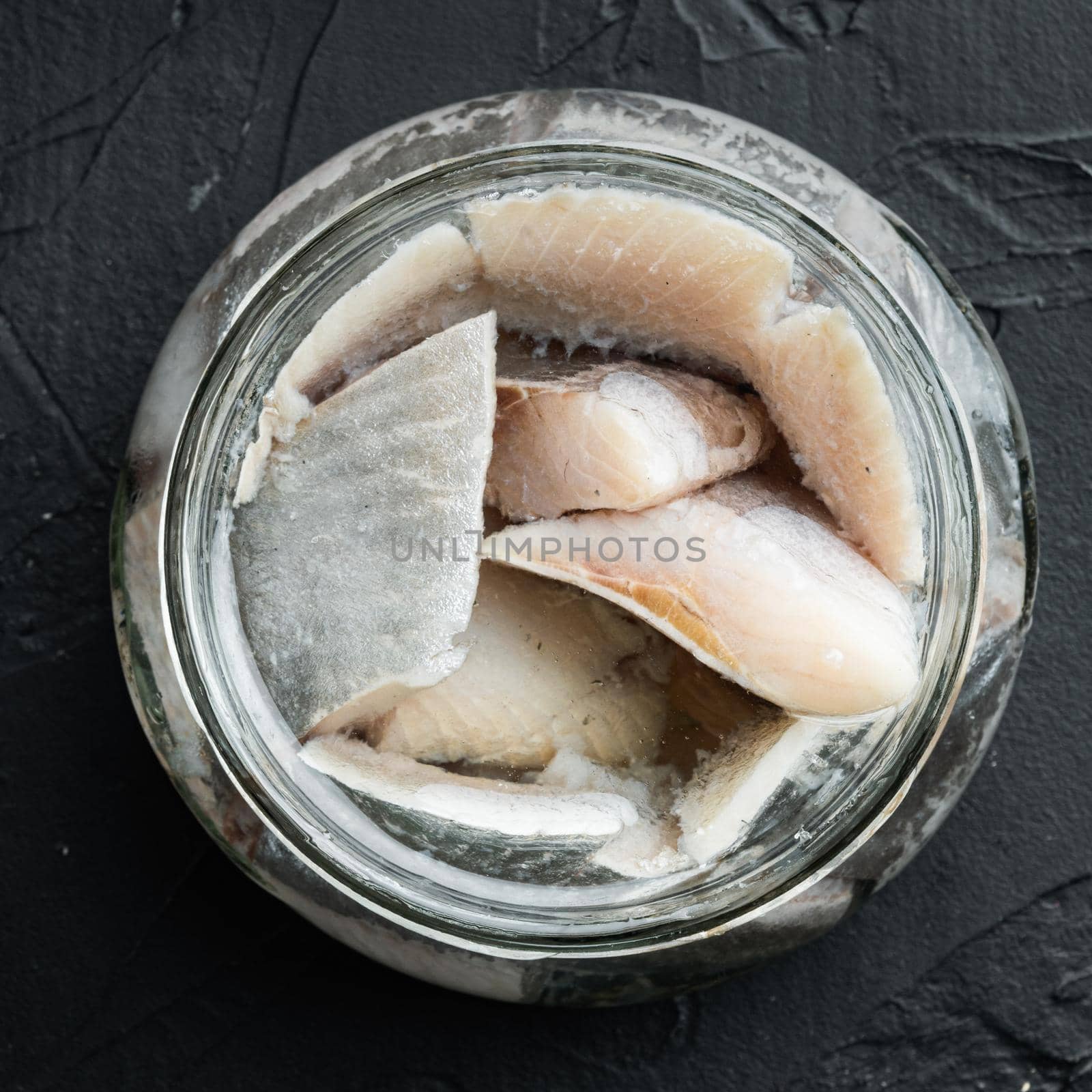 Canned Herring , fish preserves, in glass jar, on black background, top view flat lay, square format by Ilianesolenyi
