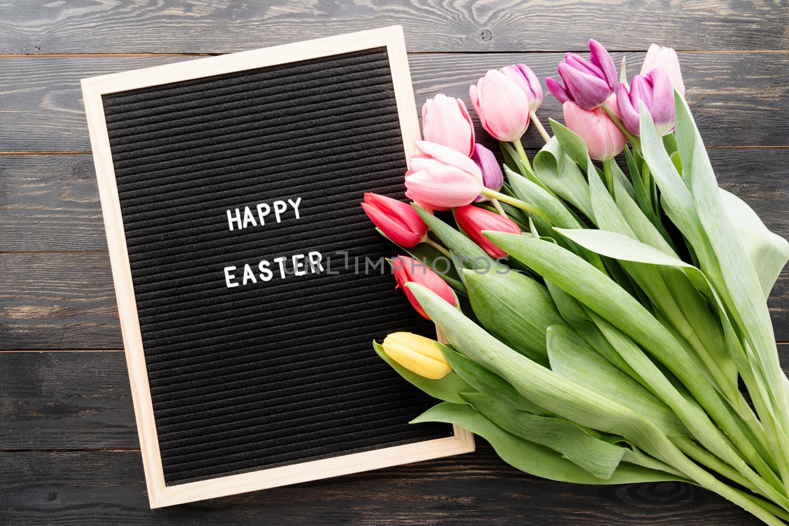 Spring concept. Bouquet of colorful tulip flowers and letter board with the words Happy Easter top view flat lay on black wooden background