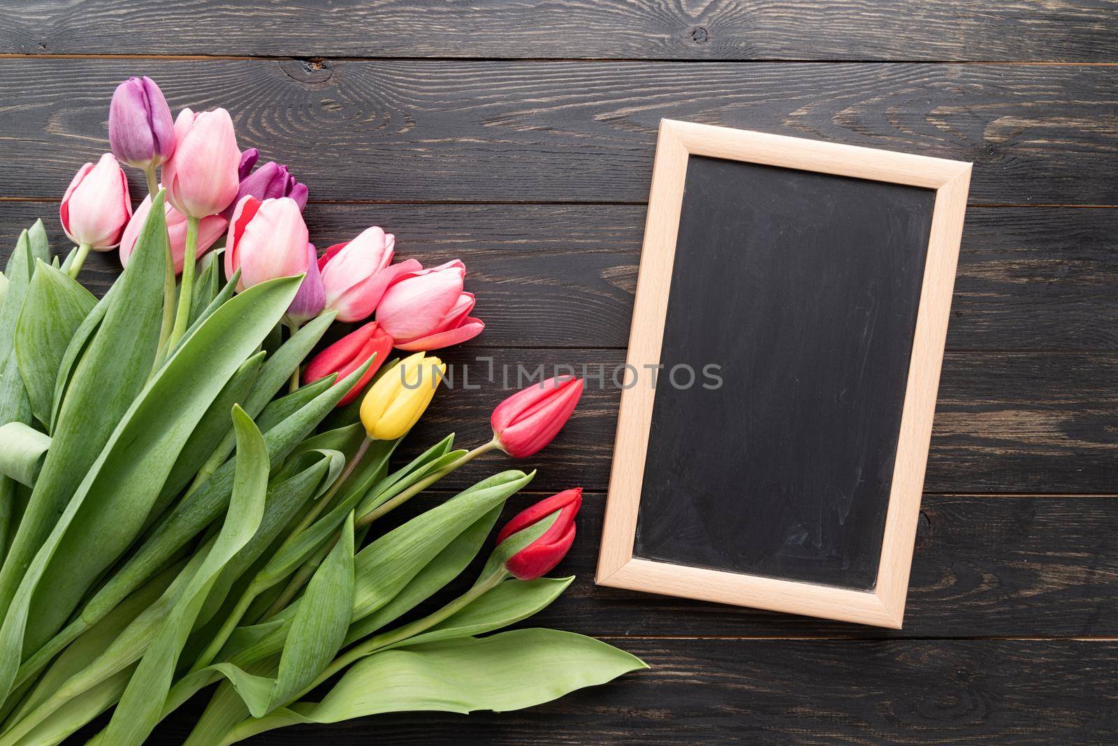 Spring, flowers concept. colorfull tulips with blank chalkboard over black wooden table background, copy space