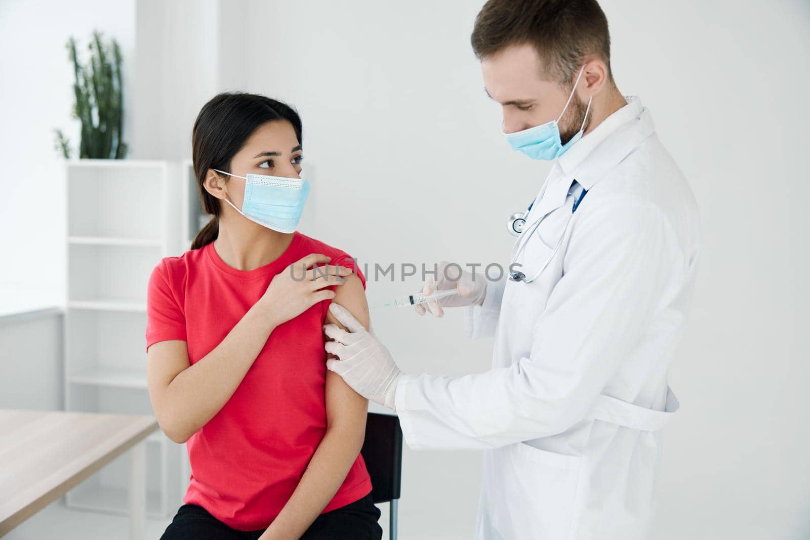 male doctor in a medical mask injecting a female patient in the shoulder. High quality photo