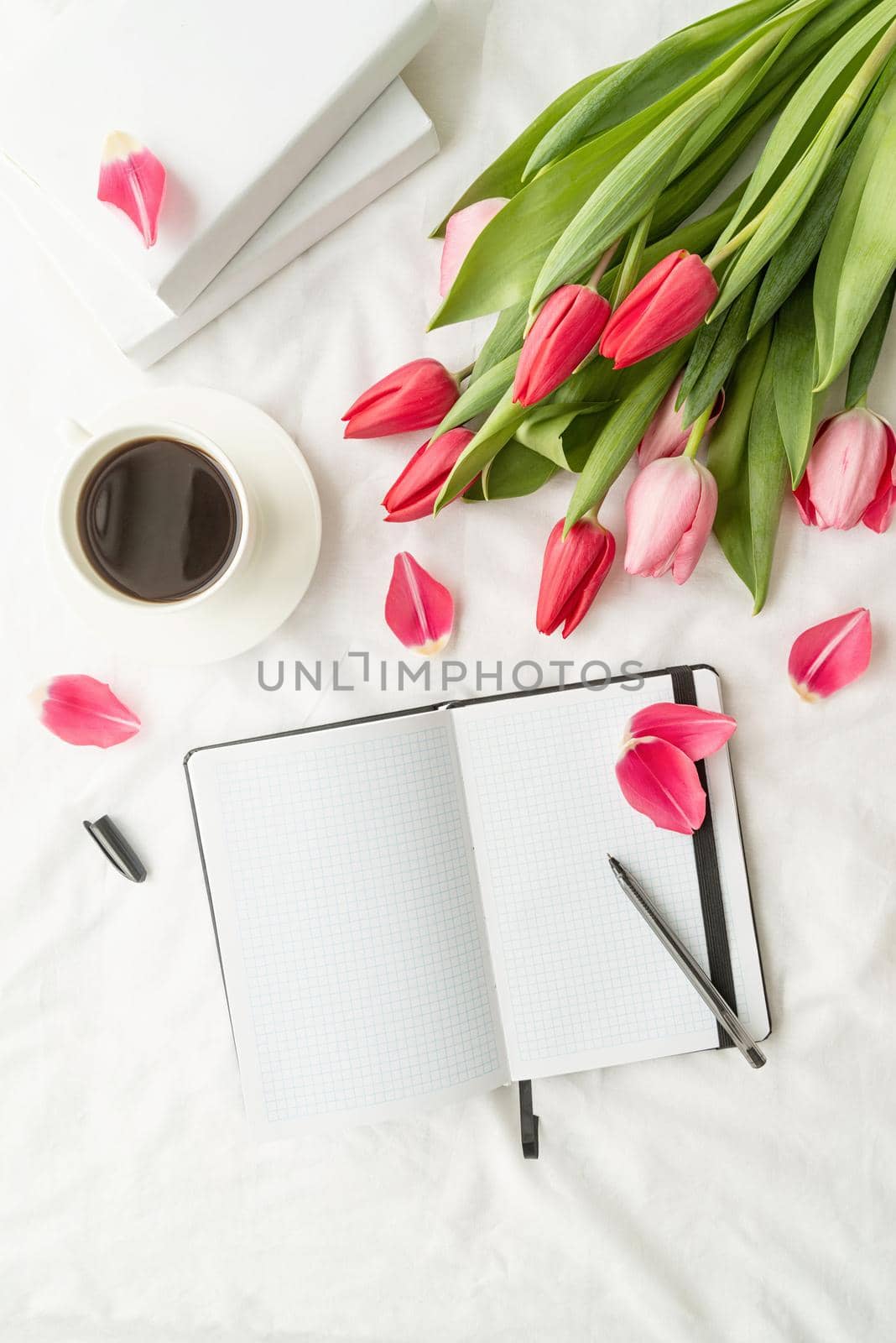 Holiday and celebration. Spring holidays. Top view of opened blank notebook with tulips and cup of coffee on white bed