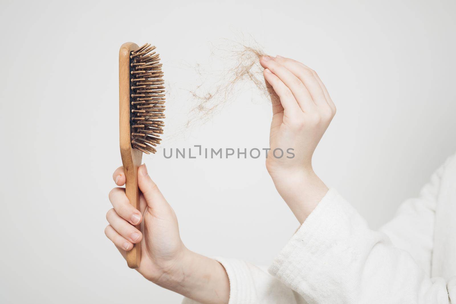 woman removes a bun of hair with a wooden comb on a light background health problems loss by SHOTPRIME