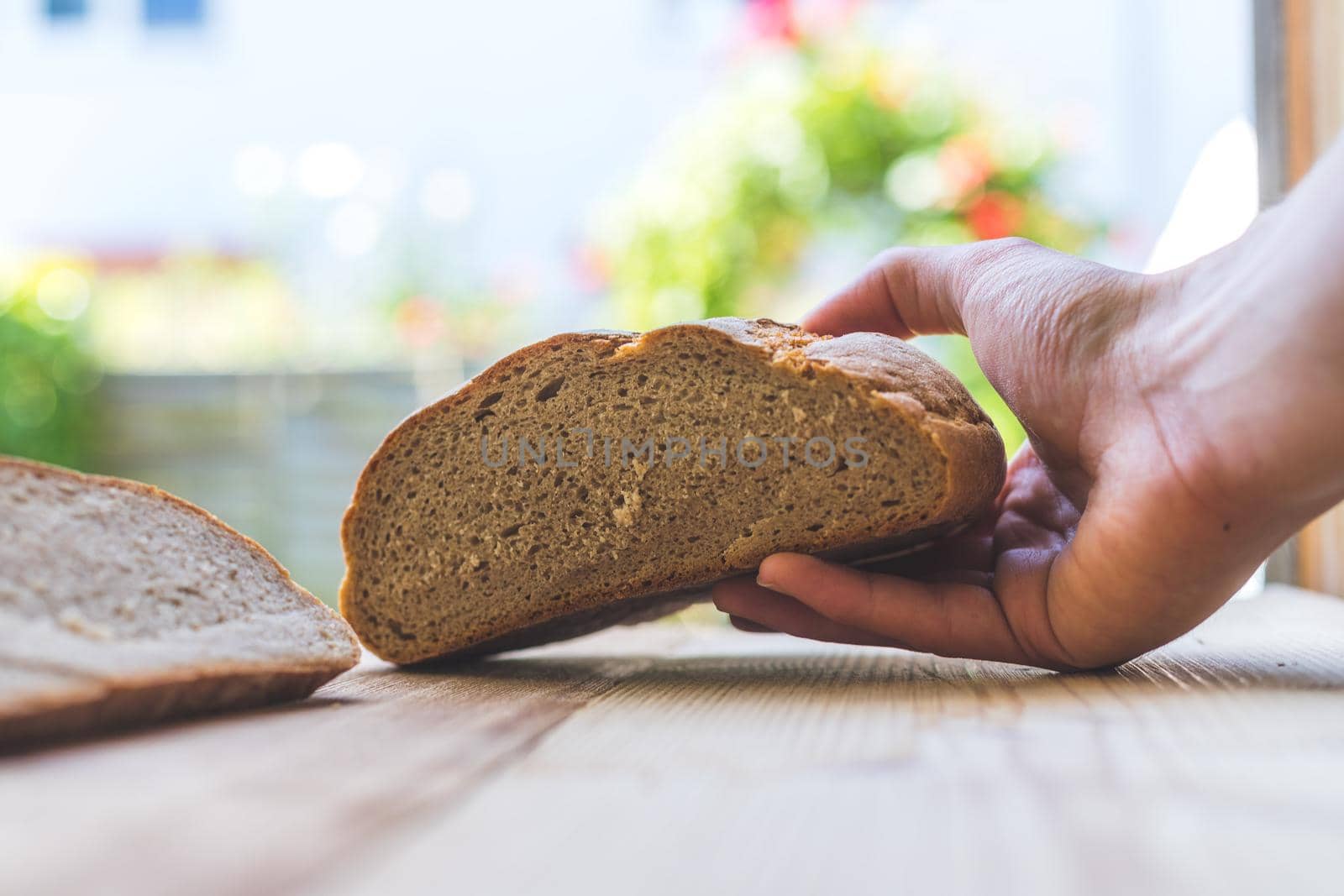 Male hand is holding a fresh rustic dark bread outdoors, breakfast