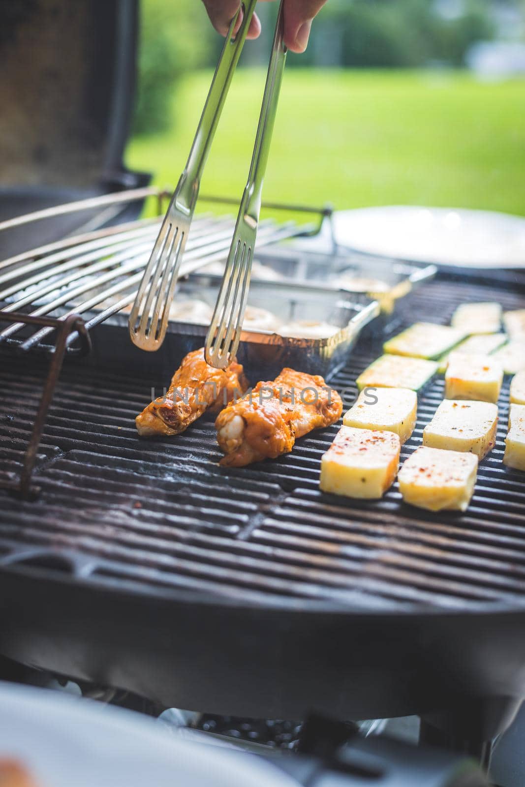 Close up of chicken wings, cheese and vegetables on gas grill. Summer time, outdoors.