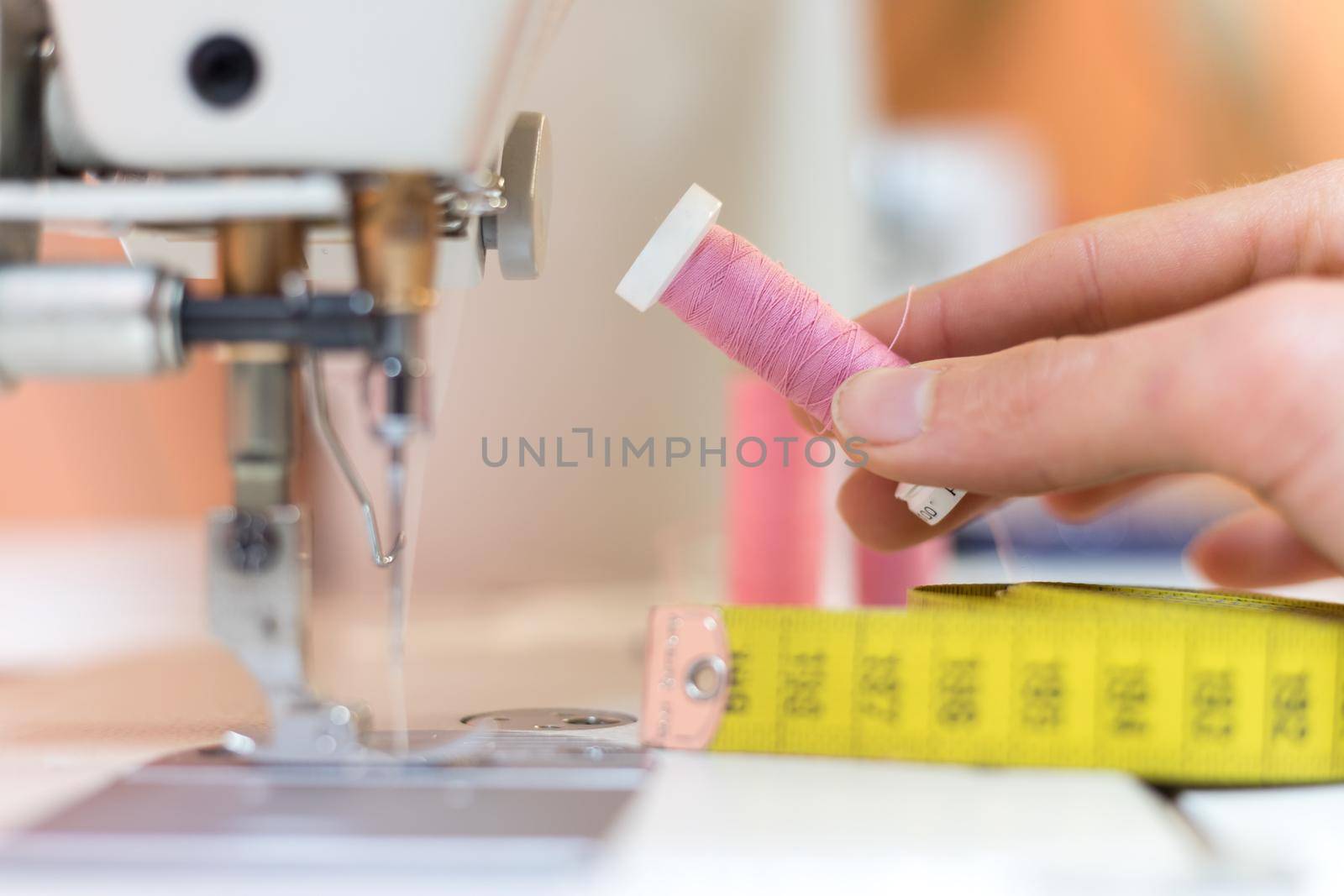 Close up of female hand holding a pink thread in a tailor workshop