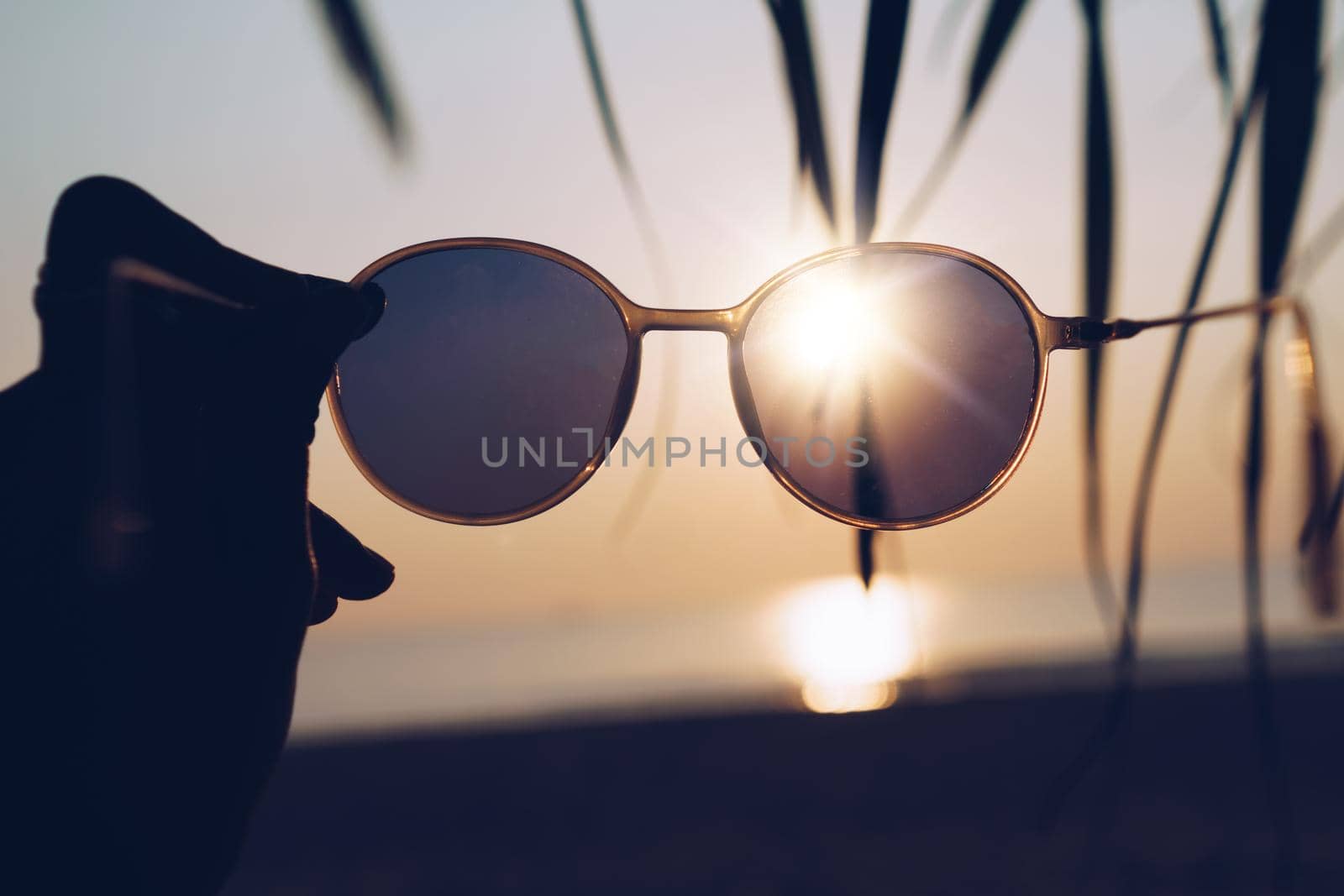 Woman hold sunglasses on sunset beach summer background with sunlight and flare.