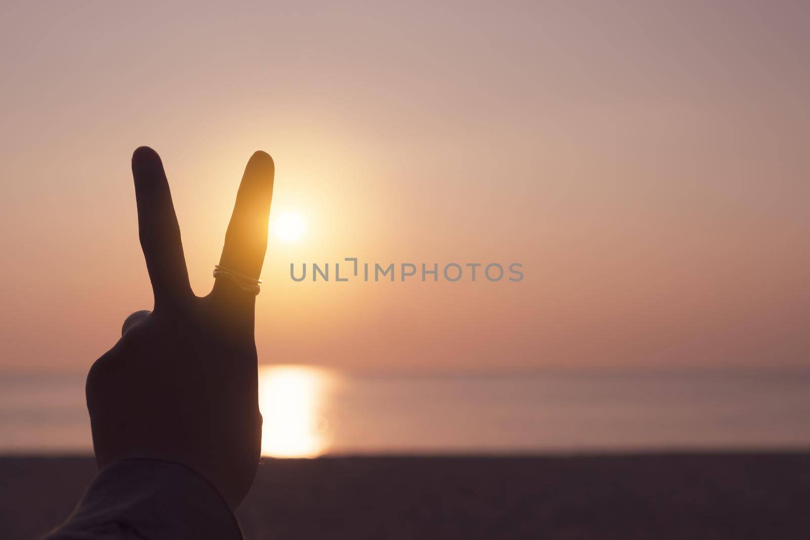 Peace out or fighting metaphor two fingers hand sign in front of a sunset. Happy people enjoying nature. 