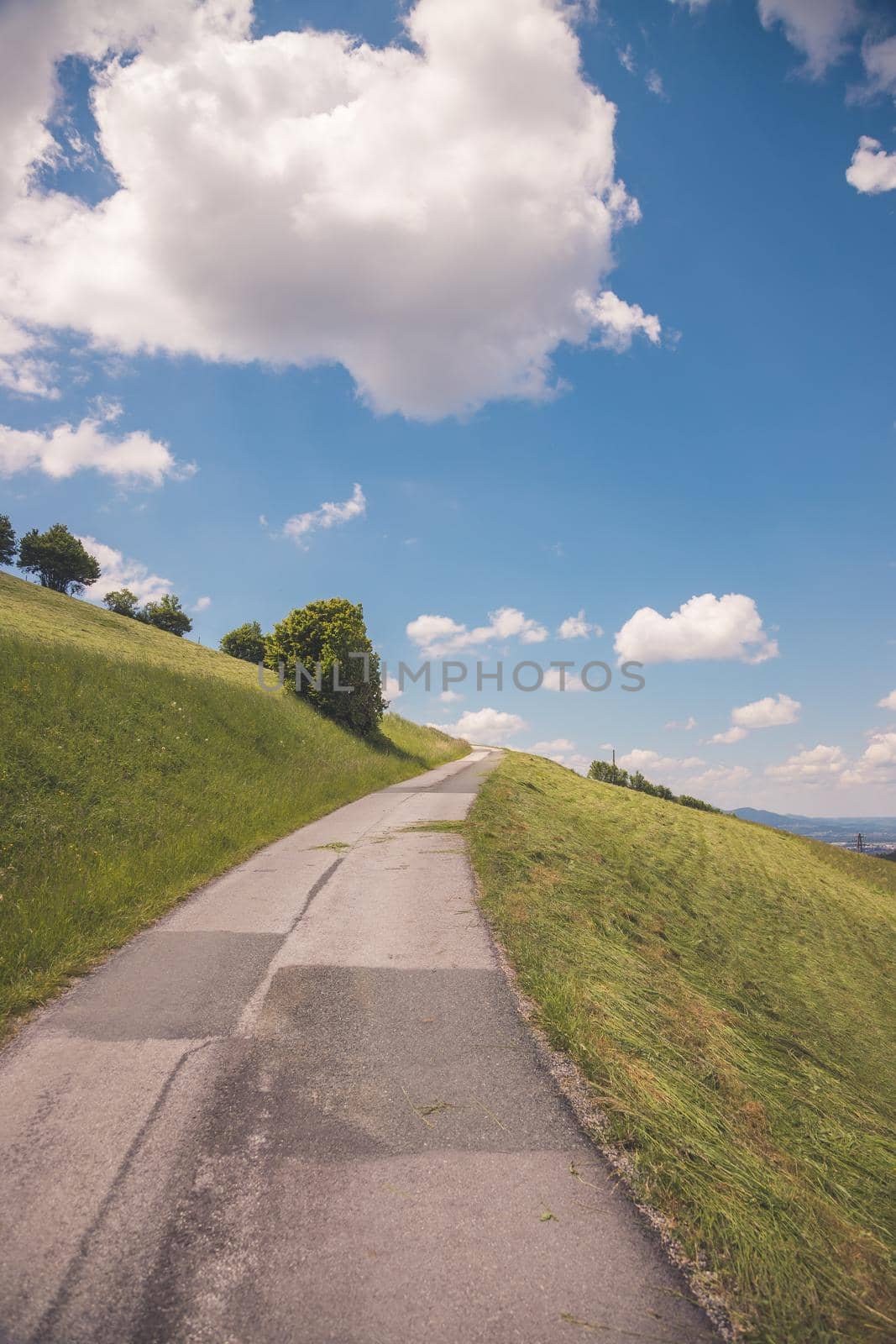 Idyllic mountain landscape, steep asphalted mountain road, green meadow and blue sky with clouds