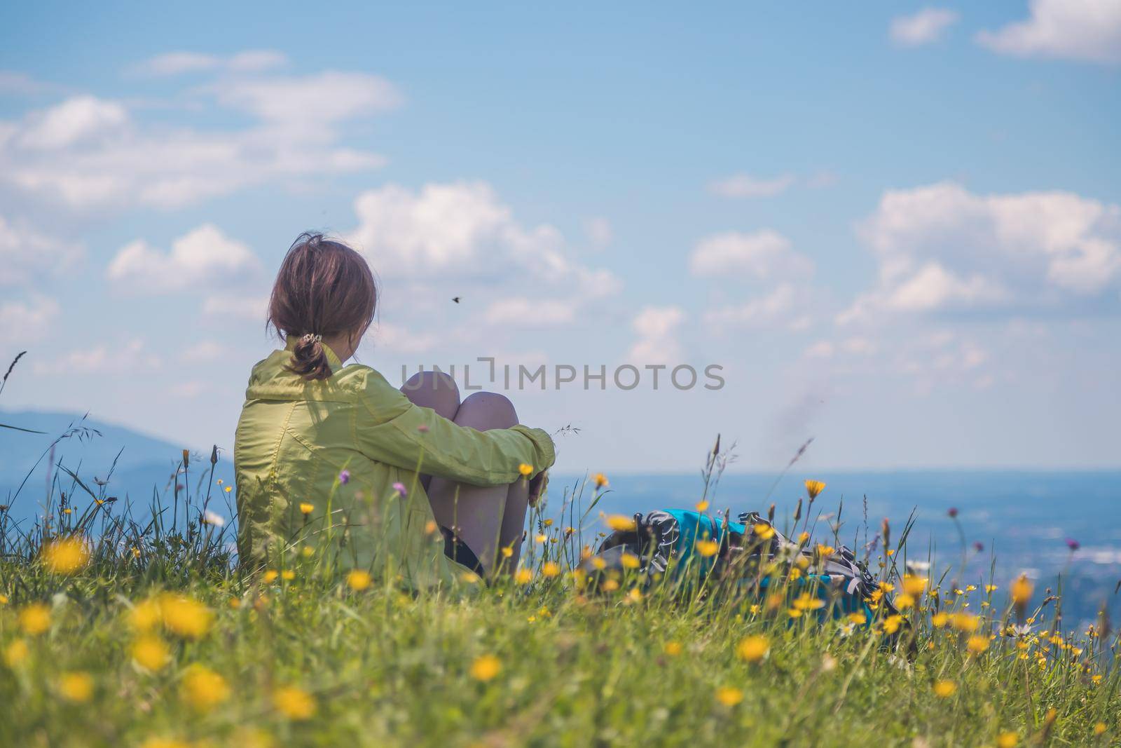 Sporty girl on a hiking trip is sitting on the meadow an enjoying the view over the far away city