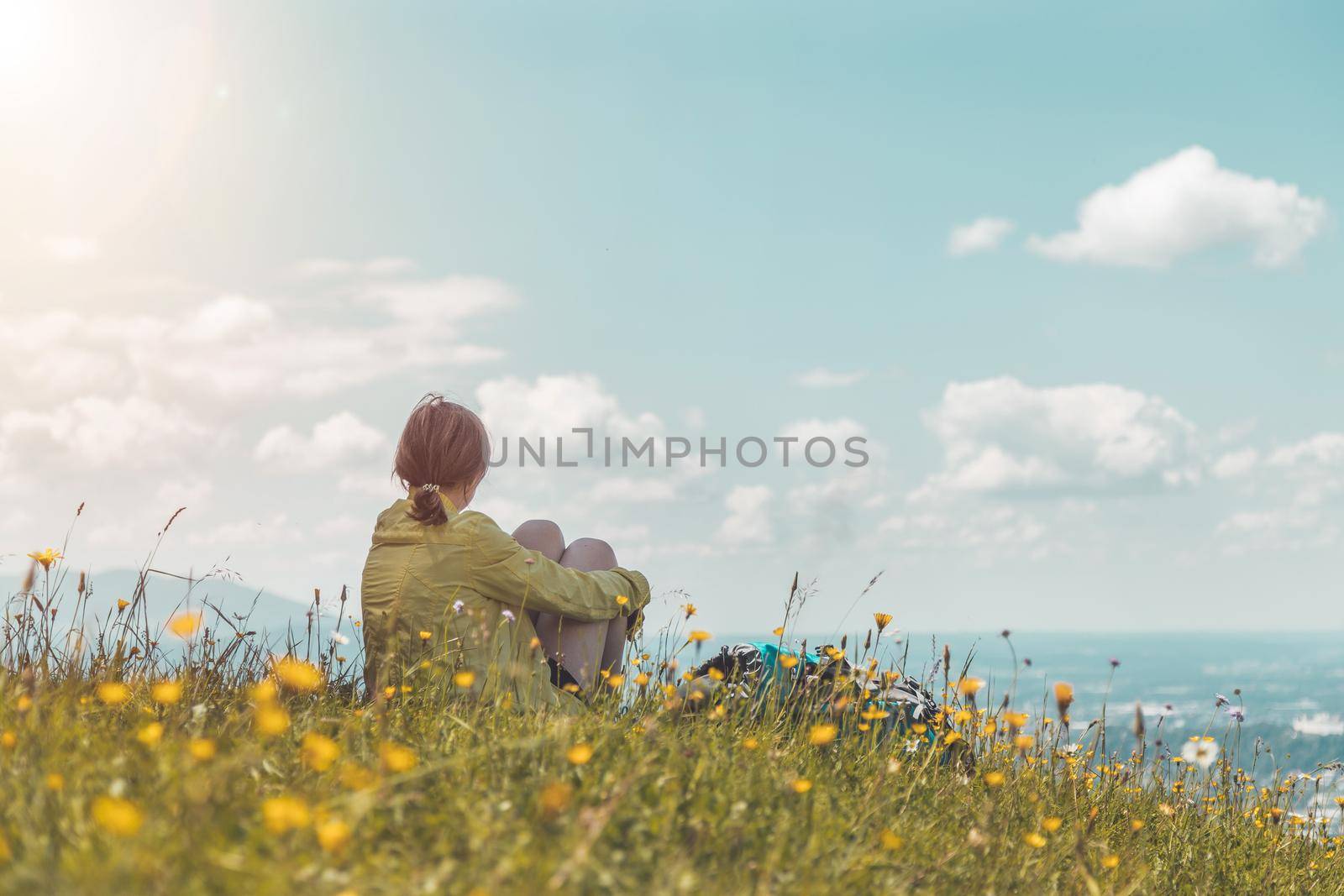 Enjoying the idyllic mountain landscape: Girl is sitting on idyllic meadow and enjoying the view over the far away city of Salzburg by Daxenbichler
