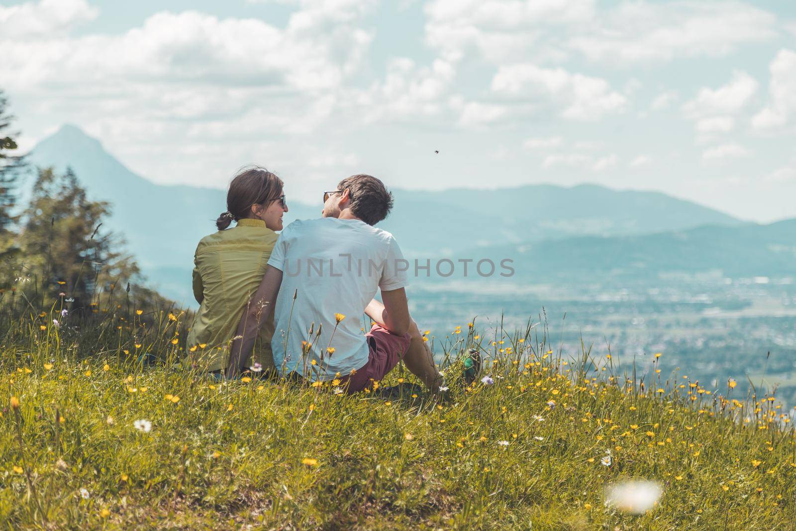 Enjoying the idyllic mountain landscape: Couple is sitting on idyllic meadow and enjoying the view over the far away city of Salzburg by Daxenbichler