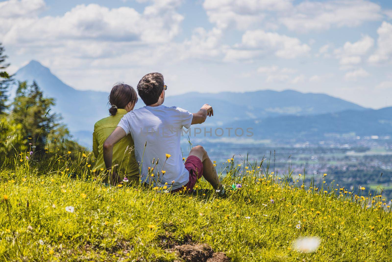 Enjoying the idyllic mountain landscape: Couple is sitting on idyllic meadow and enjoying the view over the far away city of Salzburg by Daxenbichler