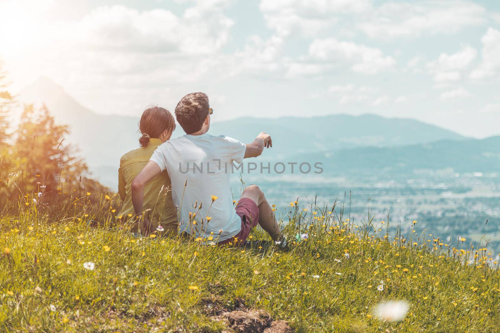 Enjoying the idyllic mountain landscape: Couple is sitting on idyllic meadow and enjoying the view over the far away city of Salzburg by Daxenbichler