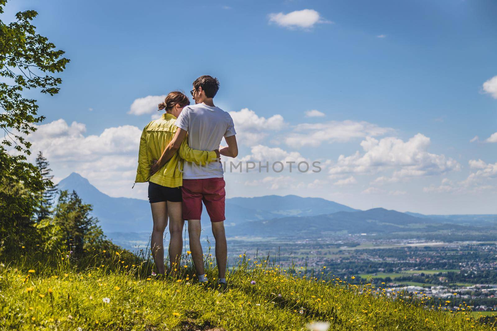 Enjoying the idyllic mountain landscape: Couple is standing on idyllic meadow and enjoying the view over the far away city of Salzburg by Daxenbichler