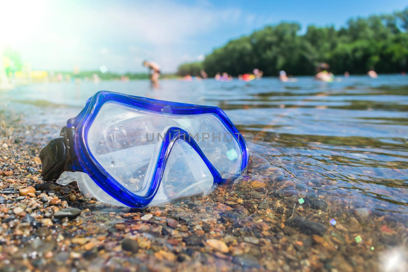 A swimming mask lies on a public beach near the water against the background of vacationing people