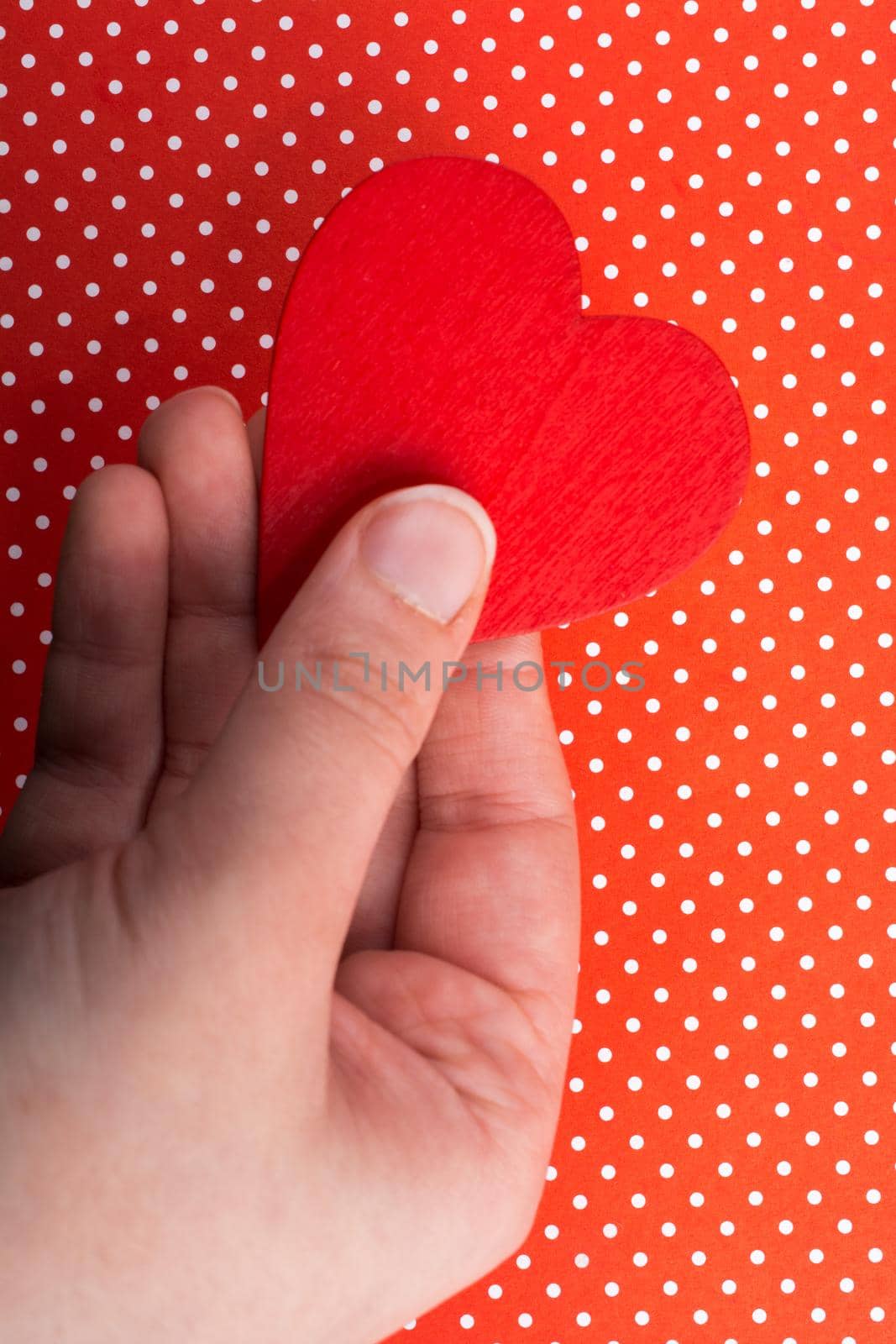 Red color heart shaped object in hand  on dotted paper