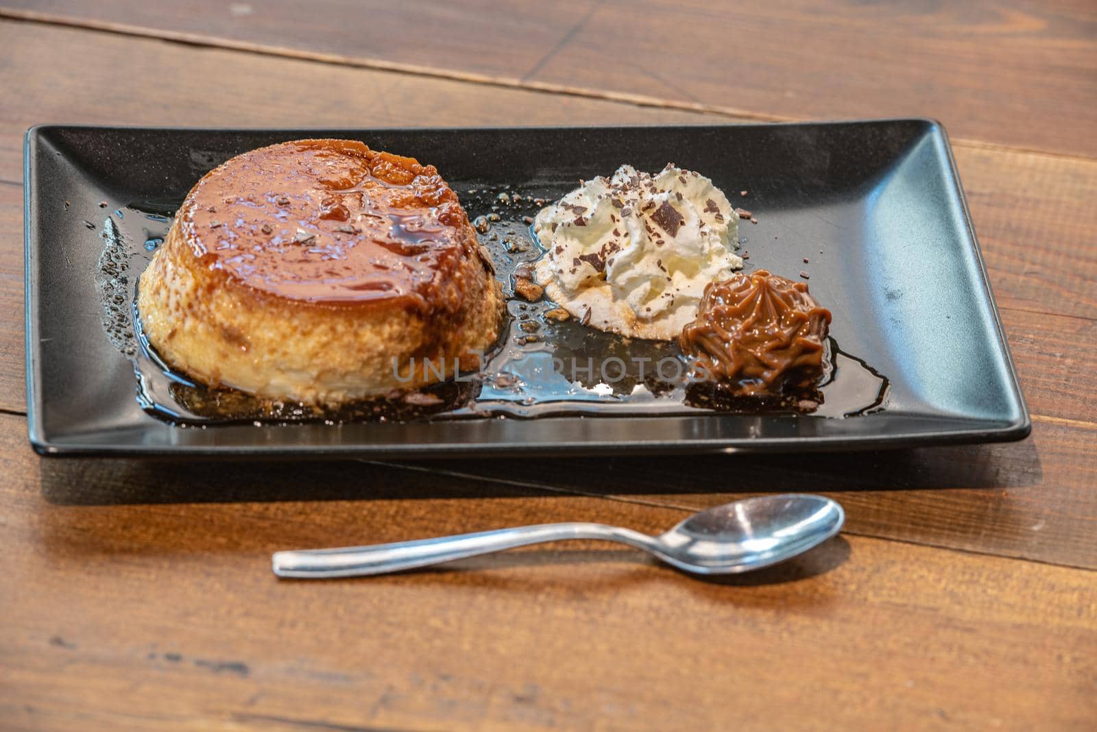 Homemade flan with cream and dulce de leche served on a black plate.