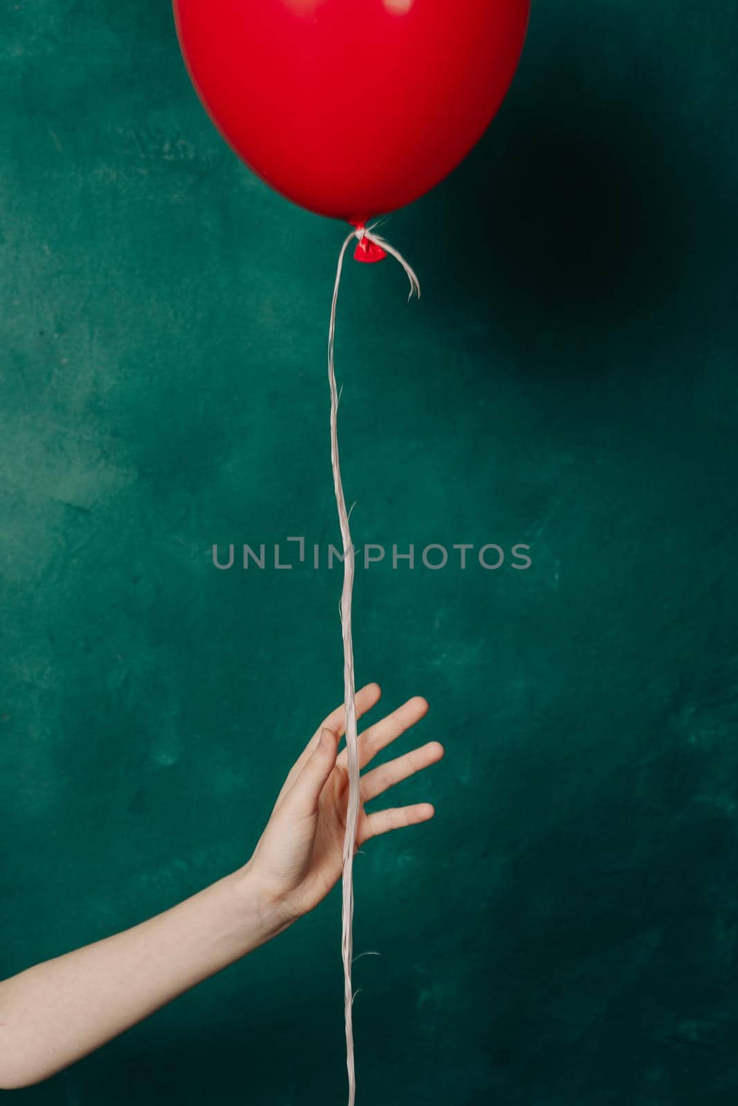 inflatable red balloon in a female hand on a green background close-up. High quality photo