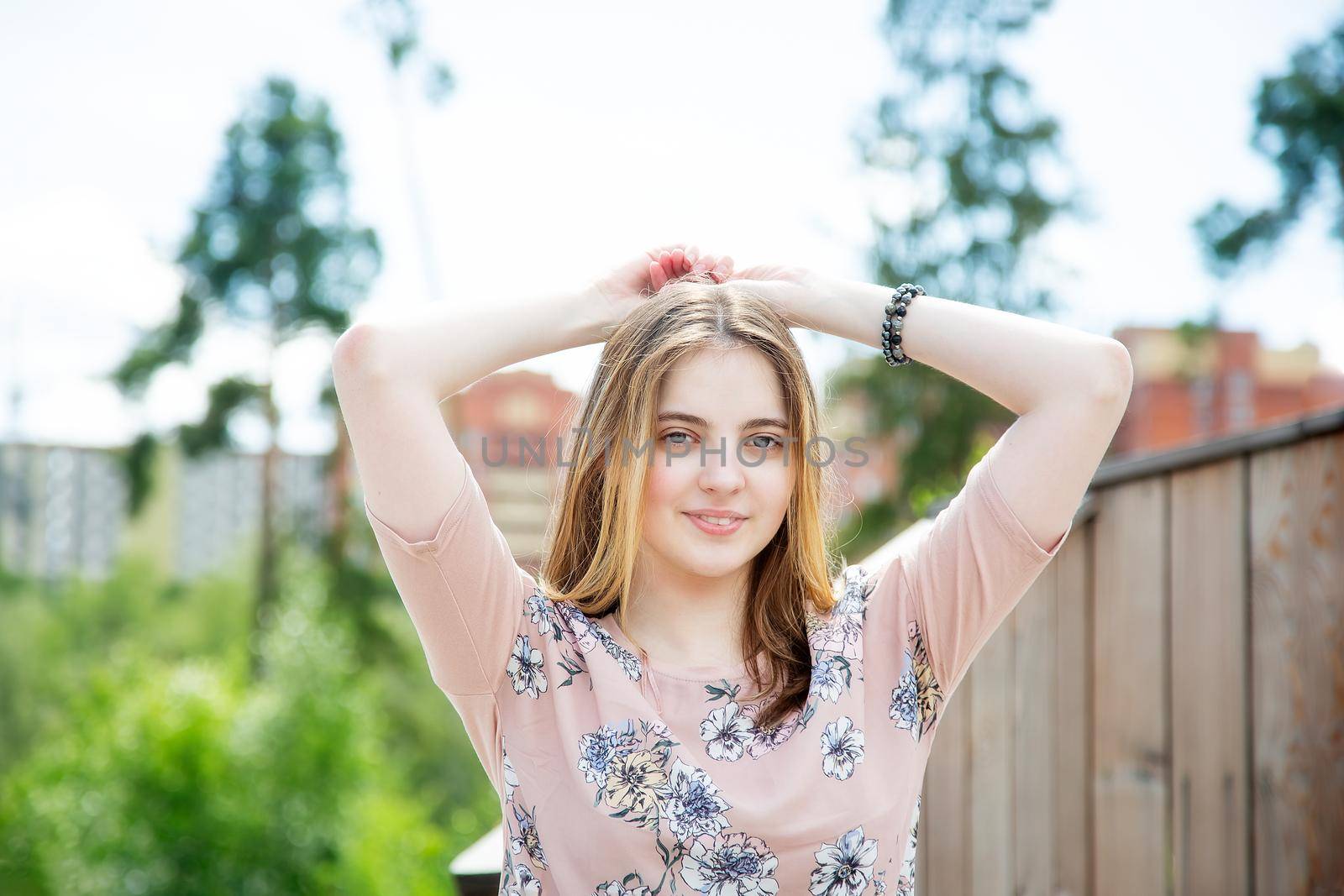 A young girl of 20 years old Caucasian appearance enjoys the sun and weather while sitting on a wooden podium in the park on a summer day.The girl is dressed in a floral T-shirt and jeans