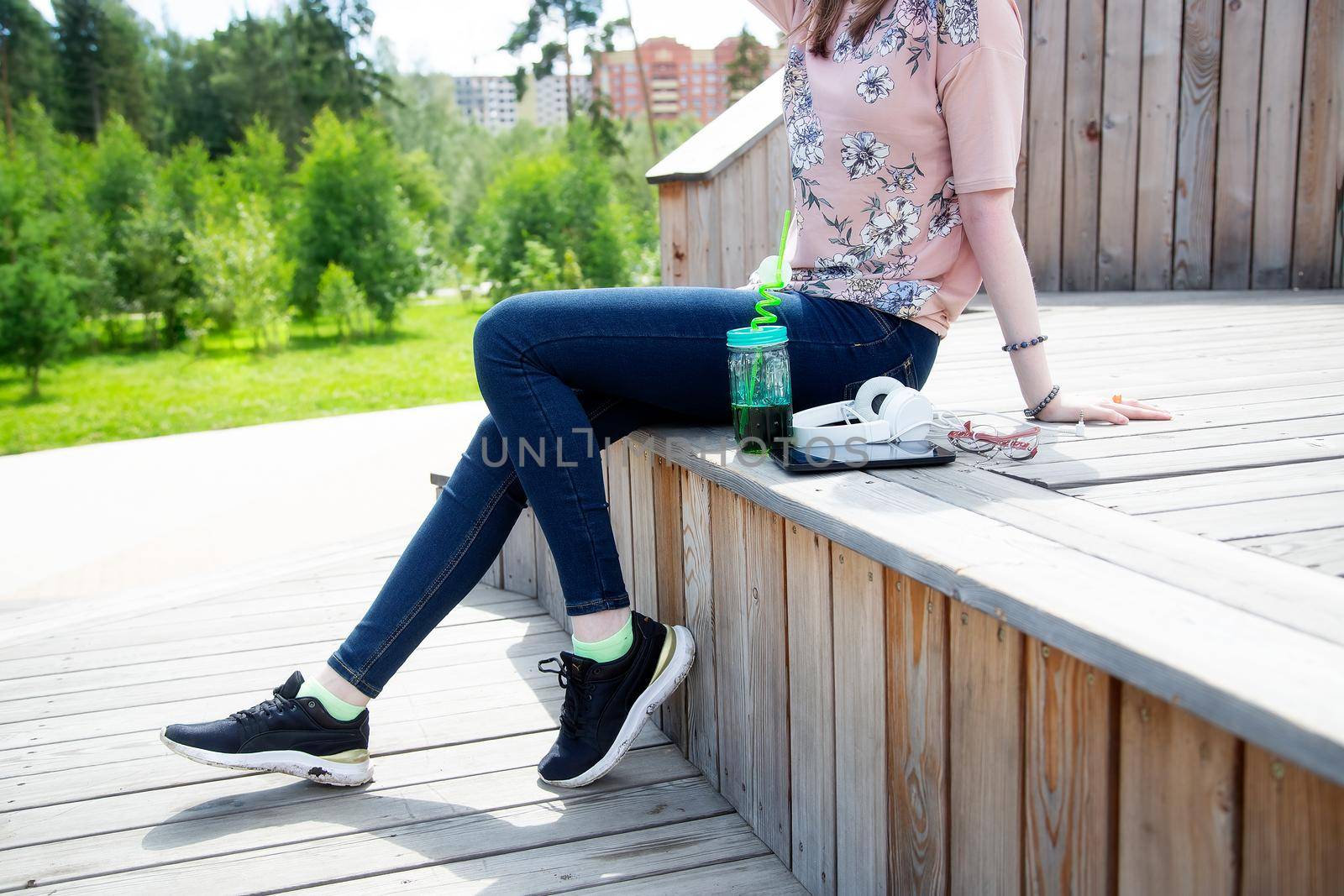 Cropped view of young girl sitting on a wooden podium in the park on a summer day.The girl is dressed in a floral T-shirt and jeans