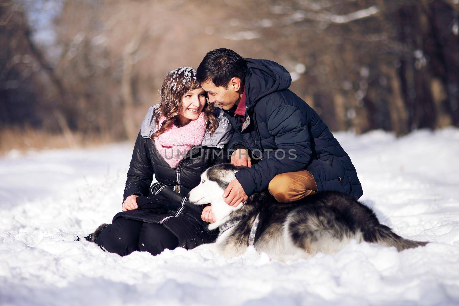 Attractive couple smiling and having fun in winter park with their siberian husky dog.