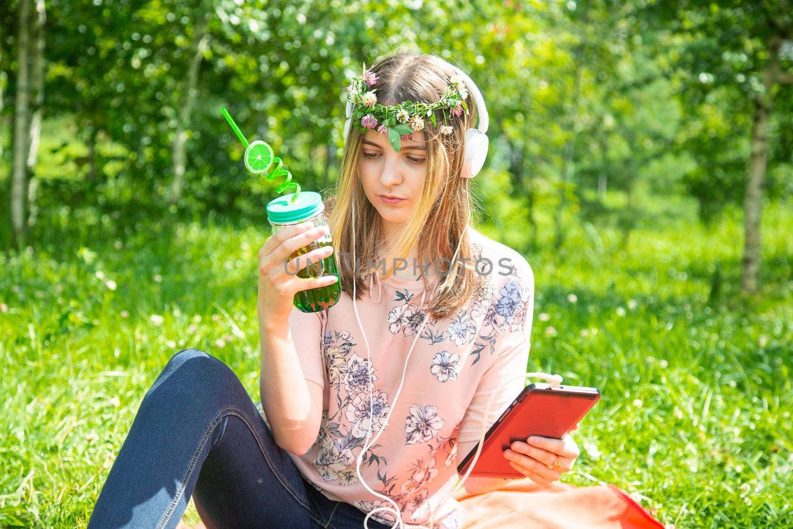 A young girl listens to music on her mobile phone and drinks smoothies in park by galinasharapova
