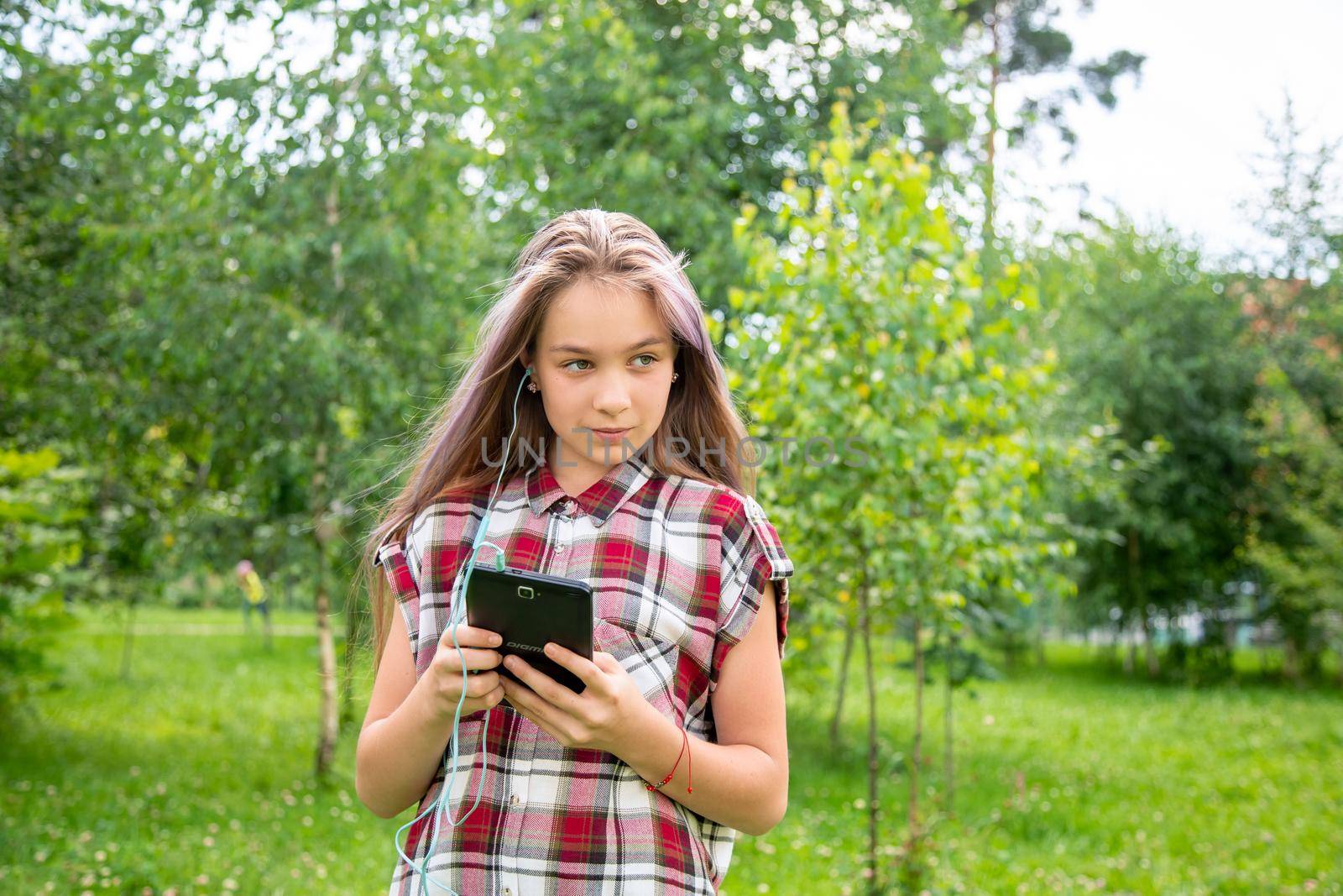 A young girl of 15 years old looks around and holds a mobile phone in the park by galinasharapova