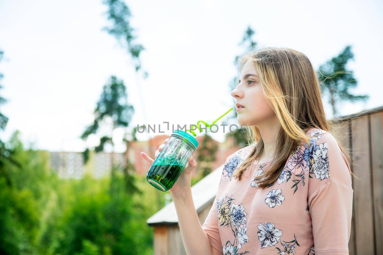 A young girl enjoys the sun and weather and drinks smoothies from a large glass by galinasharapova