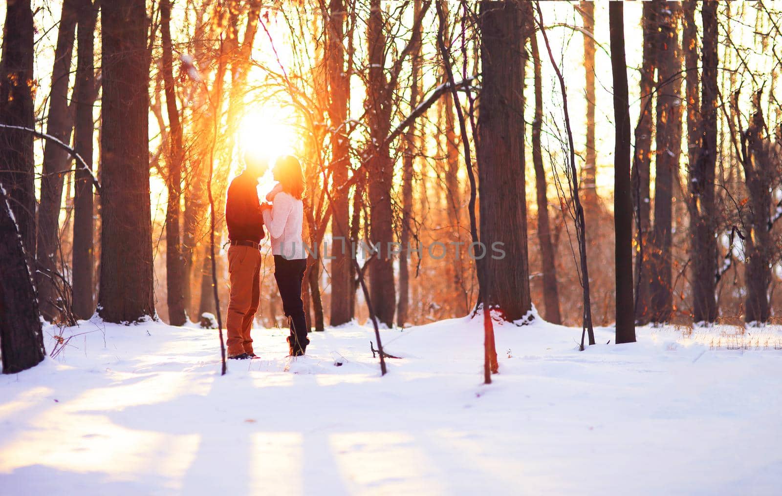 Young couple on winter holiday in a snowy forest at sunset. 