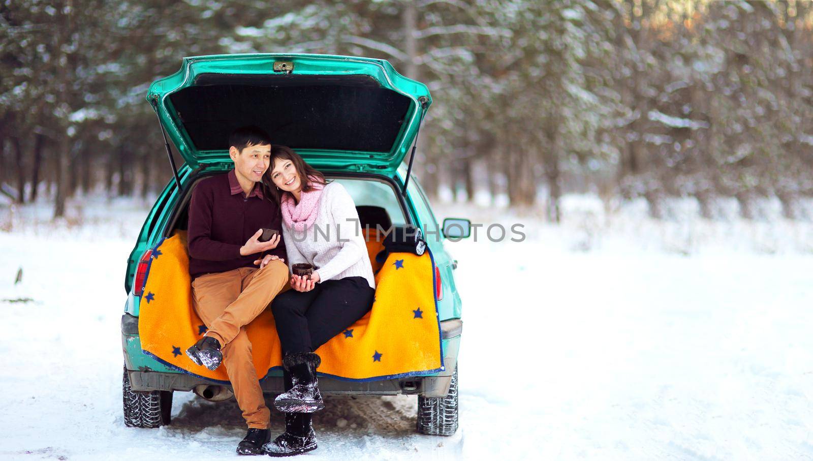 Happy couple sitting in the open trunk of a car in winter on nature by selinsmo