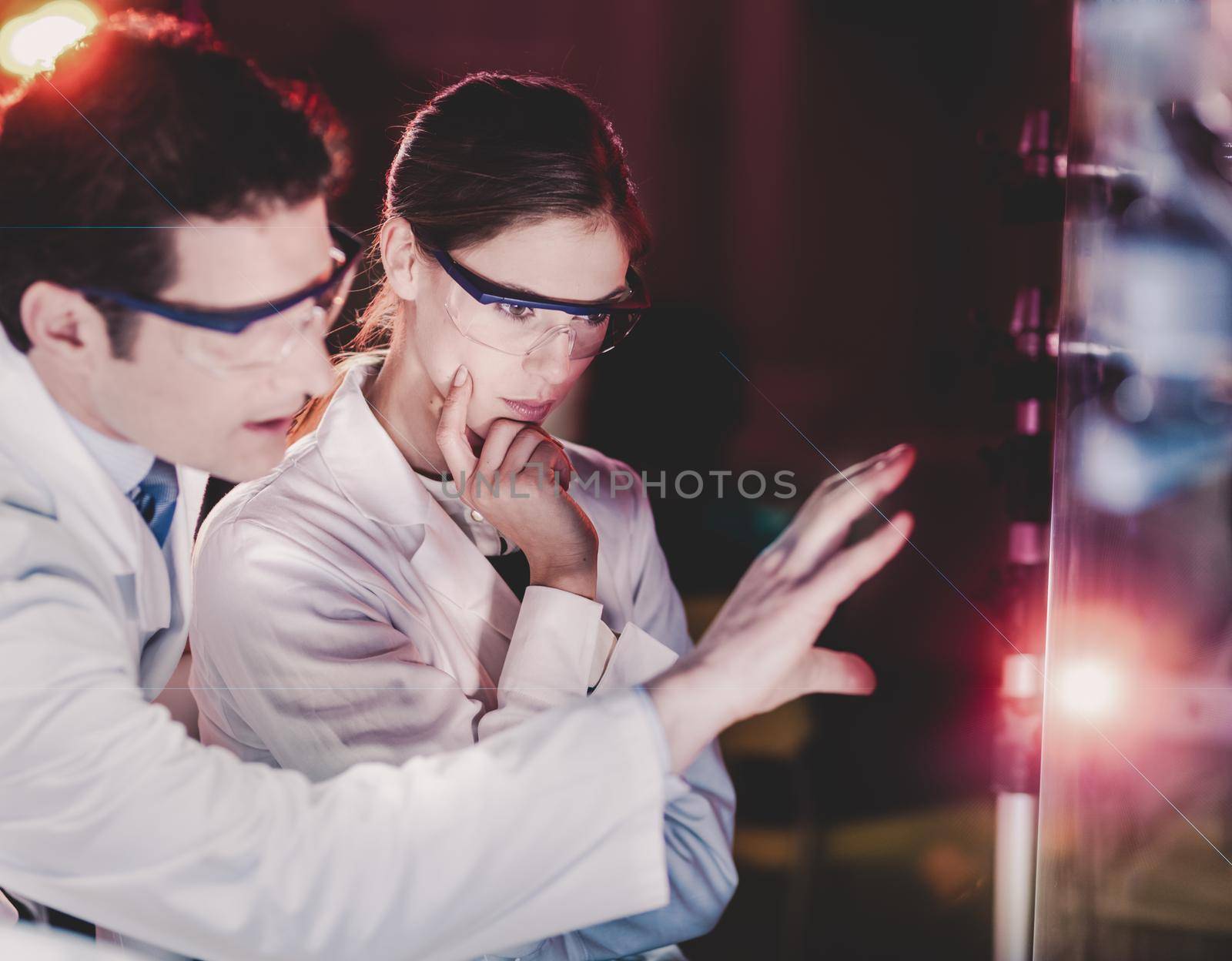 Portrait of a focused electrical engineering researchers in their working environment checking the phenomenon of breaking laser beam on the glass surface.