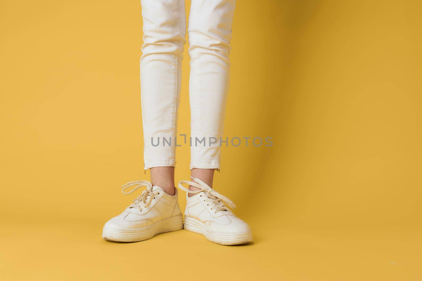 Female feet white sneakers attractive look fashion yellow background by SHOTPRIME