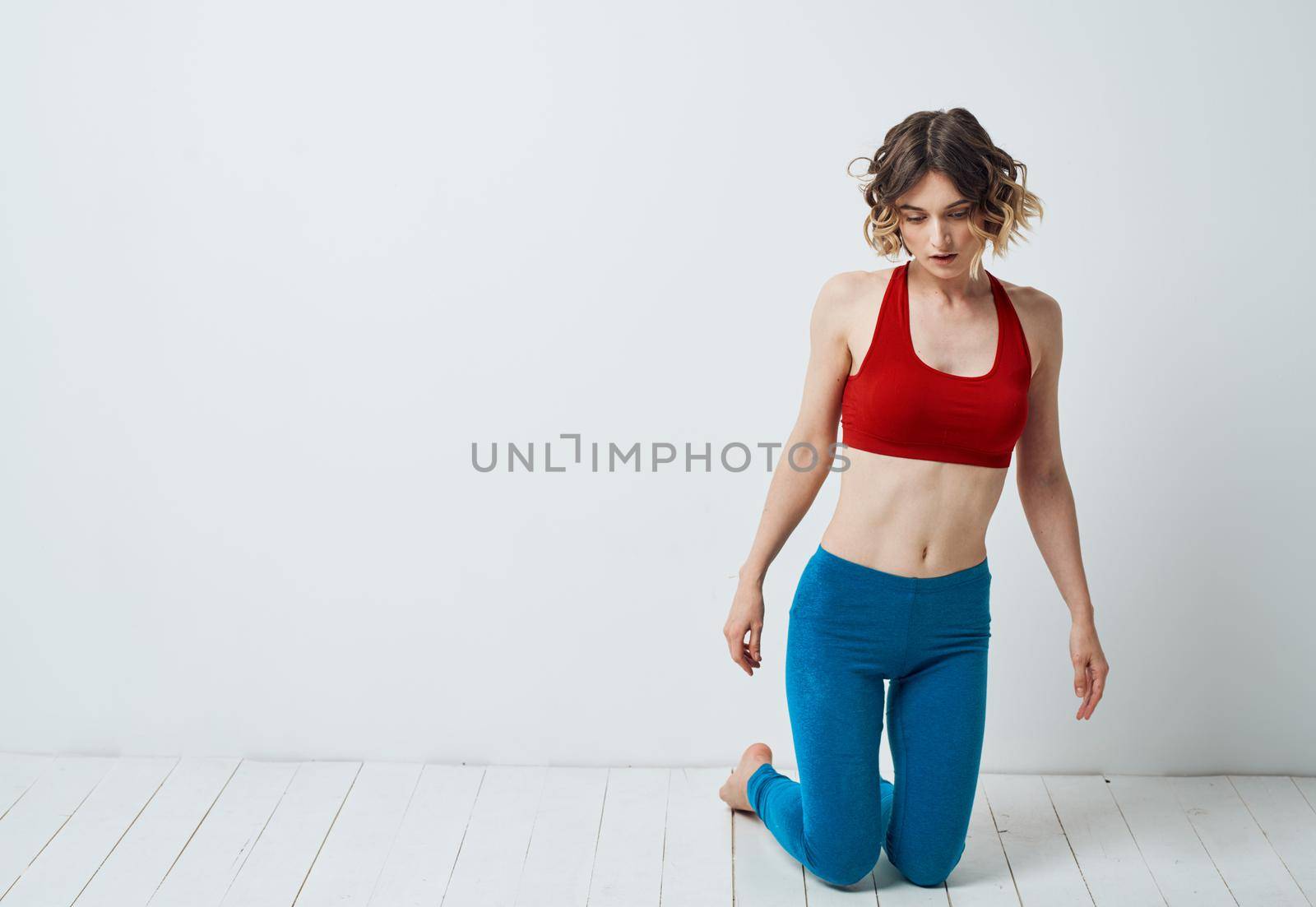 Woman Practicing Yoga In A Bright Room And Blue Leggings Red T-shirt by SHOTPRIME