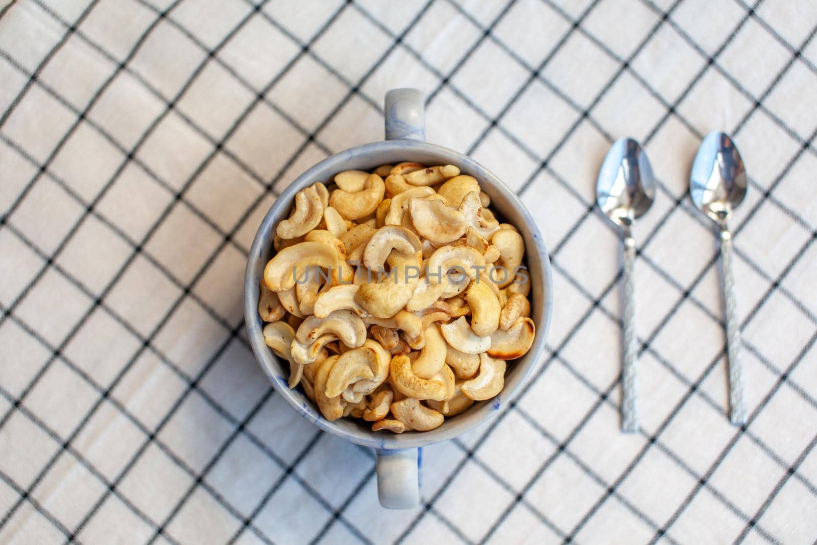 A plate of cashew nuts on a nice napkin and two spoons next to it. Delicious and healthy food for a snack. There is a place for the text.